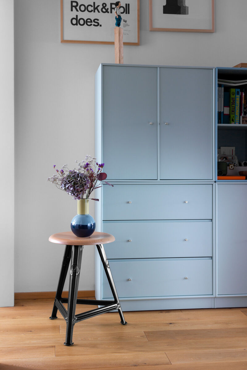 Rowac-Schemel aus Eichenholz in Mattschwarz vor einer blauen Kommode im Hintergrund, dekoriert mit einer Vase mit Blumen darauf.