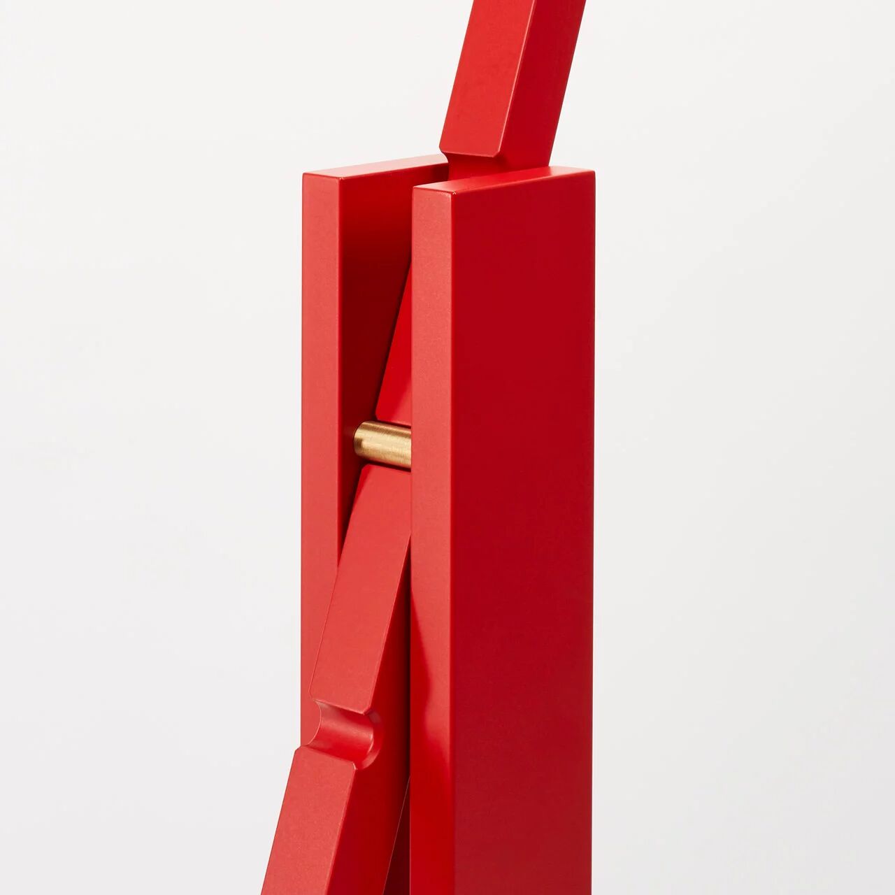 Detailaufnahme der Stehleuchte »schliephacke« von mawa design in kräftigem Rot. Sichtbar sind klar konturierte Aluminium-Elemente mit feinem, matten Finish, verbunden über ein dezentes Scharnier aus goldfarbenem Metall vor hellem Hintergrund. Präzise Verarbeitung und modernes, geometrisches Design.