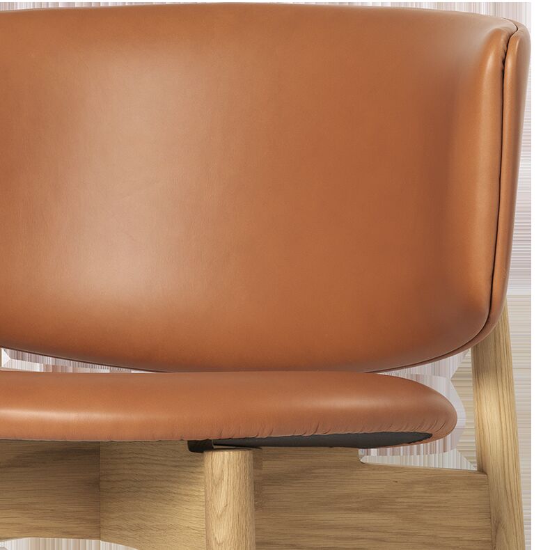 Detailansicht eines hochwertigen Loungesessels der Marke ferm LIVING, Modell Herman Lounge Chair. Die Sitzfläche und Rückenlehne sind aus cognacfarbenem Anilinleder gefertigt, der Rahmen besteht aus FSC®-zertifizierter heller Eiche. Abgerundete Formen und klare Linien im skandinavischen Designstil.