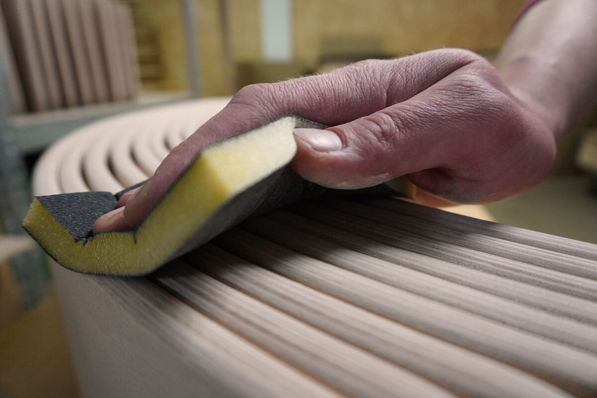 Eine Nahaufnahme einer Hand, die ein rundes Balance Board aus Holz mit einem Schleifschwamm glättet. Das Holz des Balance Boards hat eine geölte Oberfläche und zeigt deutlich die Maserung des Holzes.