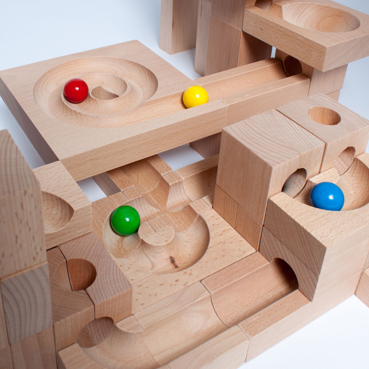 Holz-Kugelbahn mit mehreren Bausteinen in natürlicher Holzfarbe. Kugeln in verschiedenen Farben – rot, blau, gelb und grün – rollen durch Bahnen. Geeignet für Kinder, um kreative Spiellandschaften zu bauen und die Motorik zu fördern.
