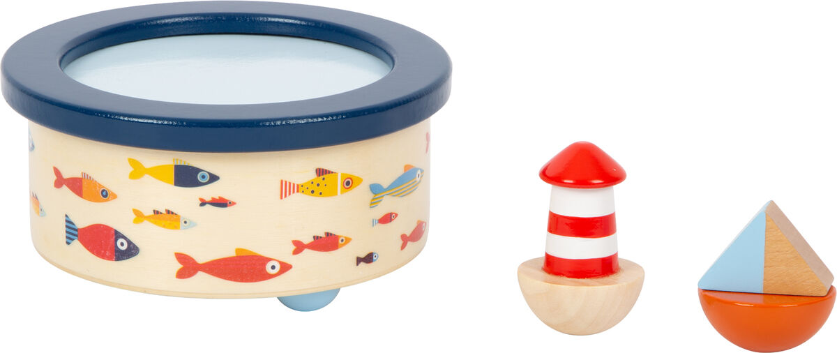 Eine Spieluhr namens 'Großer Ozean' mit maritimem Design. Die Spieluhr ist rund und aus Holz gefertigt, mit kleinen bunten Fischen darauf. Neben der Spieluhr befinden sich ein kleiner Holz-Leuchtturm und ein kleines Holz-Boot.