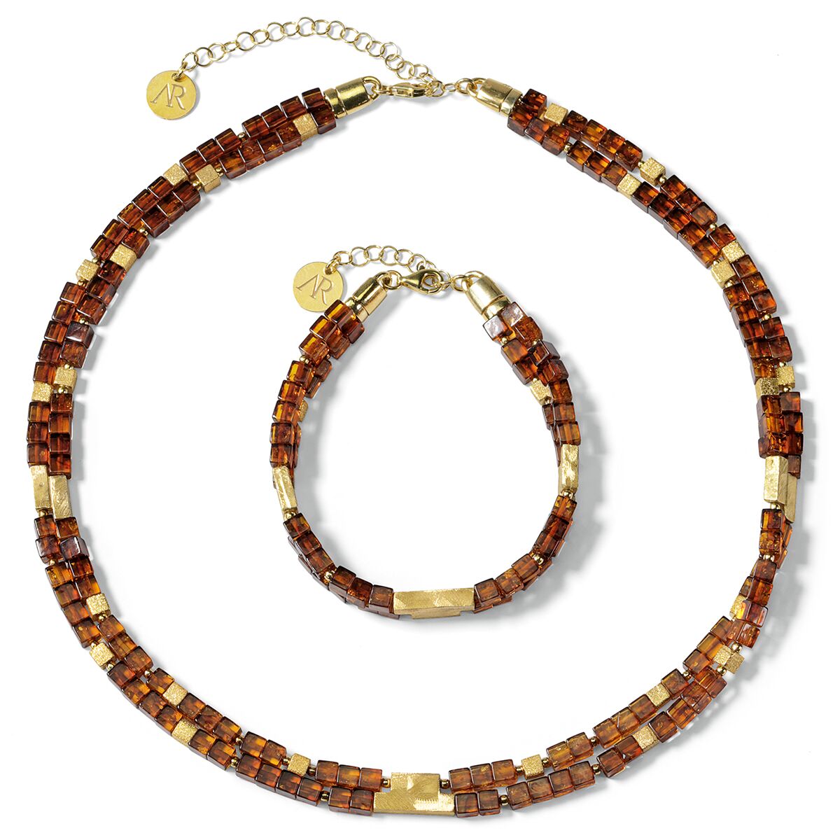 Bernstein-Schmuckset »Annabele« von Ars mundi bestehend aus einer Kette und einem Armband aus eckigen, polierten Bernsteinen und 925er-Sterlingsilber-Elementen. Die Schmuckstücke sind goldfarben akzentuiert, verfügen über Verlängerungsketten mit Markenanhänger und liegen auf weißem Hintergrund.