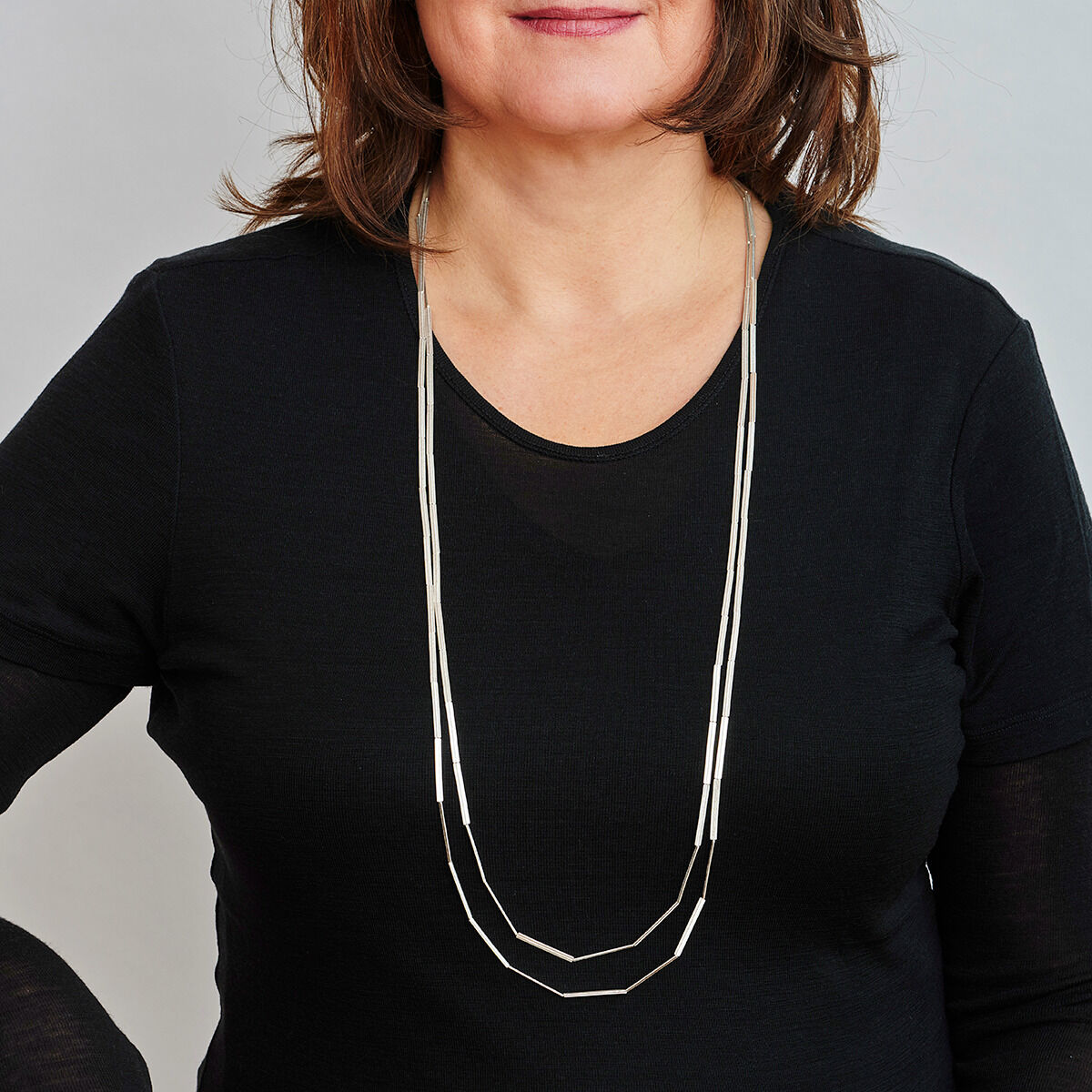 Eine Frau trägt eine lange, elegante Silberkette mit einem Streifenmuster und einem schwarzen Oberteil.