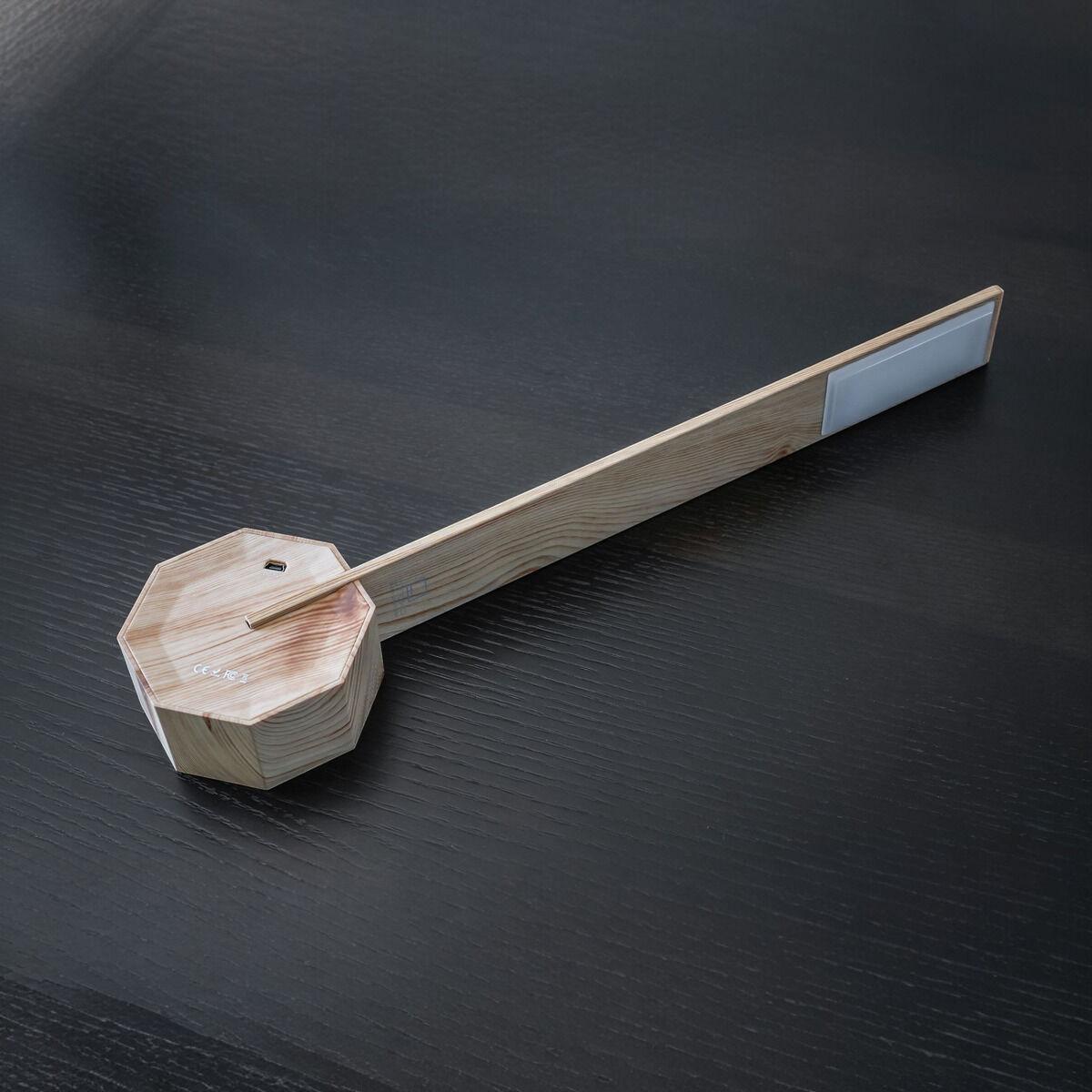 Moderne, minimalistische Tischlampe aus Holz in Form eines Oktagons mit LED-Beleuchtung auf schwarzer Oberfläche.