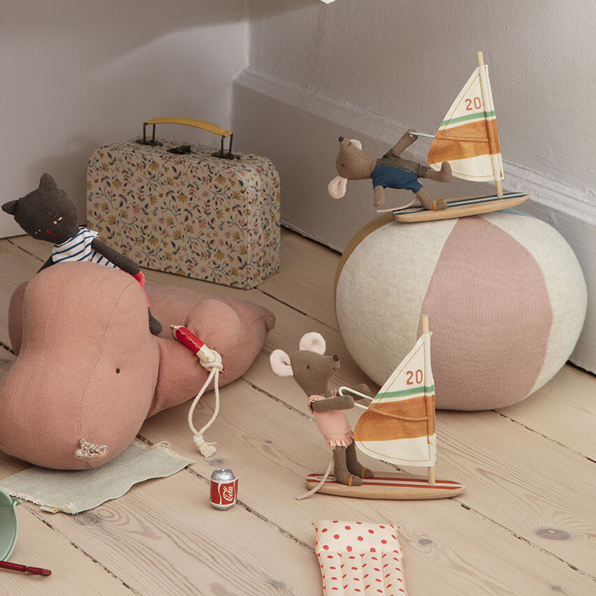 Stoffmäuse mit Surfbrett als Dekoration und Spielzeug in einem Kinderzimmer mit anderen verspielten Elementen wie einem Koffer und einem großen Ball.