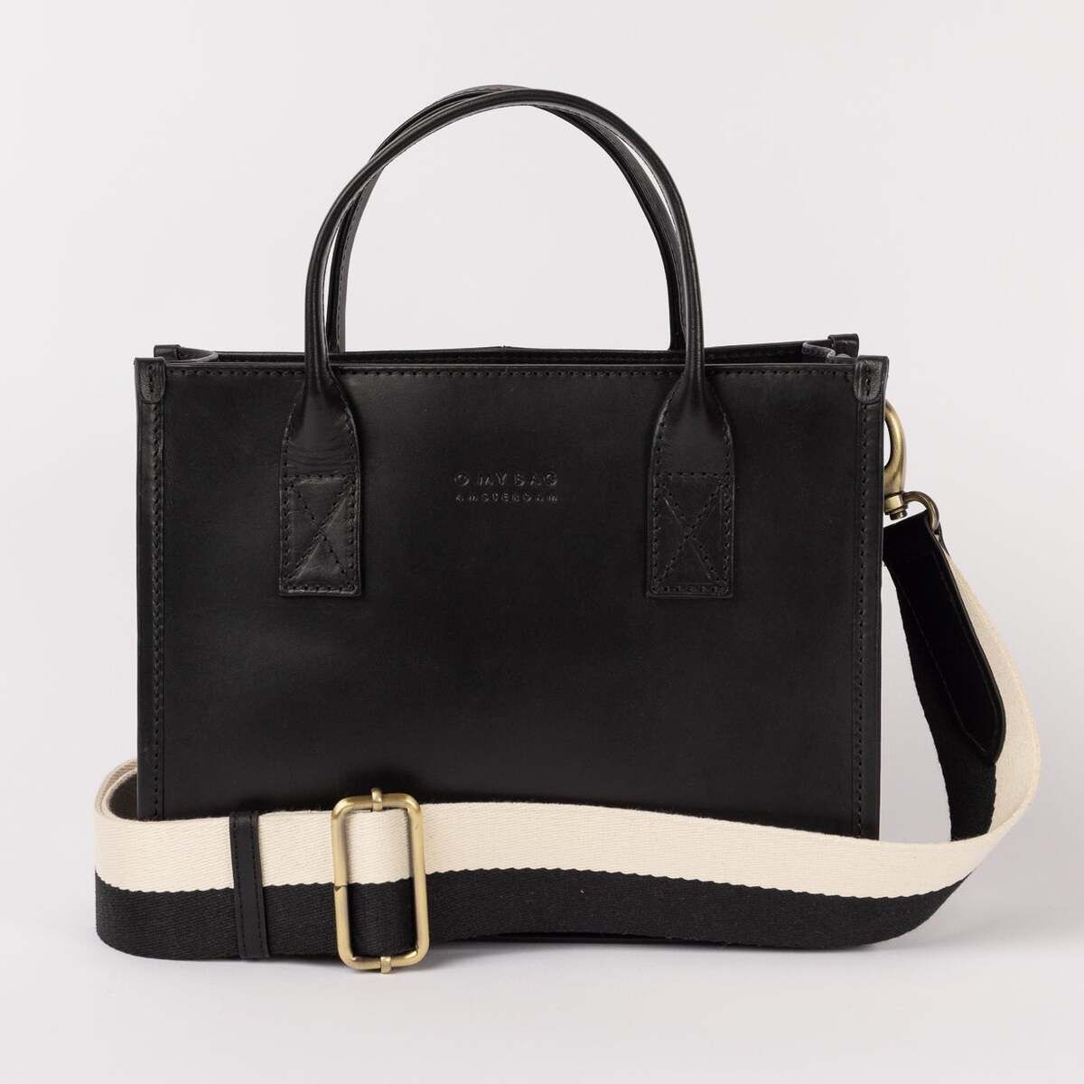 Schwarze Ledertasche »Jackie Midi« mit zwei Henkeln und einem abnehmbaren, breiten Schulterriemen in Schwarz-Weiß. Die Tasche steht vor neutralem Hintergrund und zeichnet sich durch ein minimalistisches, elegantes Design aus.