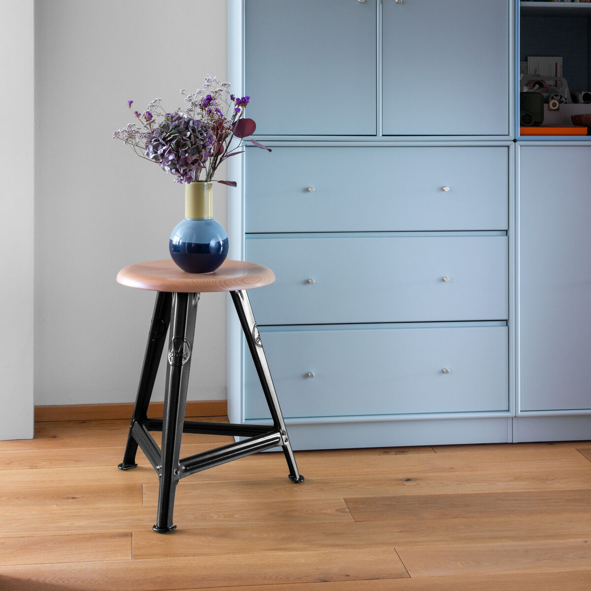 Rowac-Schemel aus Eichenholz in Mattschwarz vor einer blauen Kommode im Hintergrund, dekoriert mit einer Vase mit Blumen darauf.