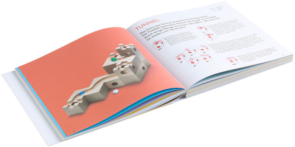 Ein aufgeschlagenes Buch zur Kugelbahn »CUBORO - DAS BUCH« zeigt Bauanleitungen und Illustrationen für kreative Projekte mit Holzspielzeug.