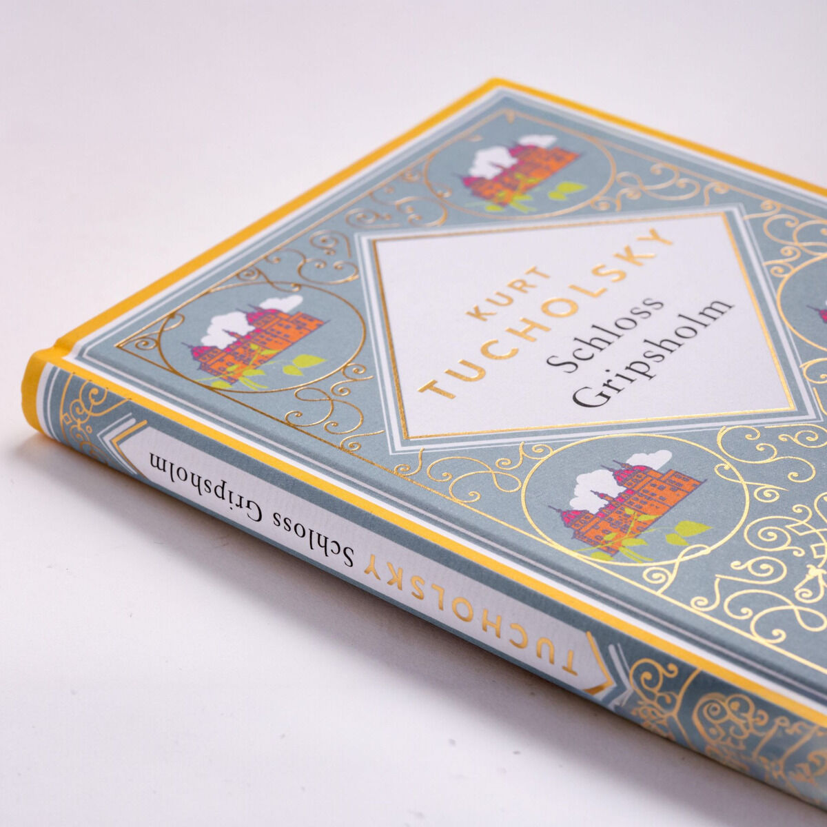 Das Bild zeigt das Buchcover von 'Schloss Gripsholm' von Kurt Tucholsky. Das Design ist nostalgisch mit gelben und blauen Verzierungen und Illustrationen eines Schlosses in rot und weiß.