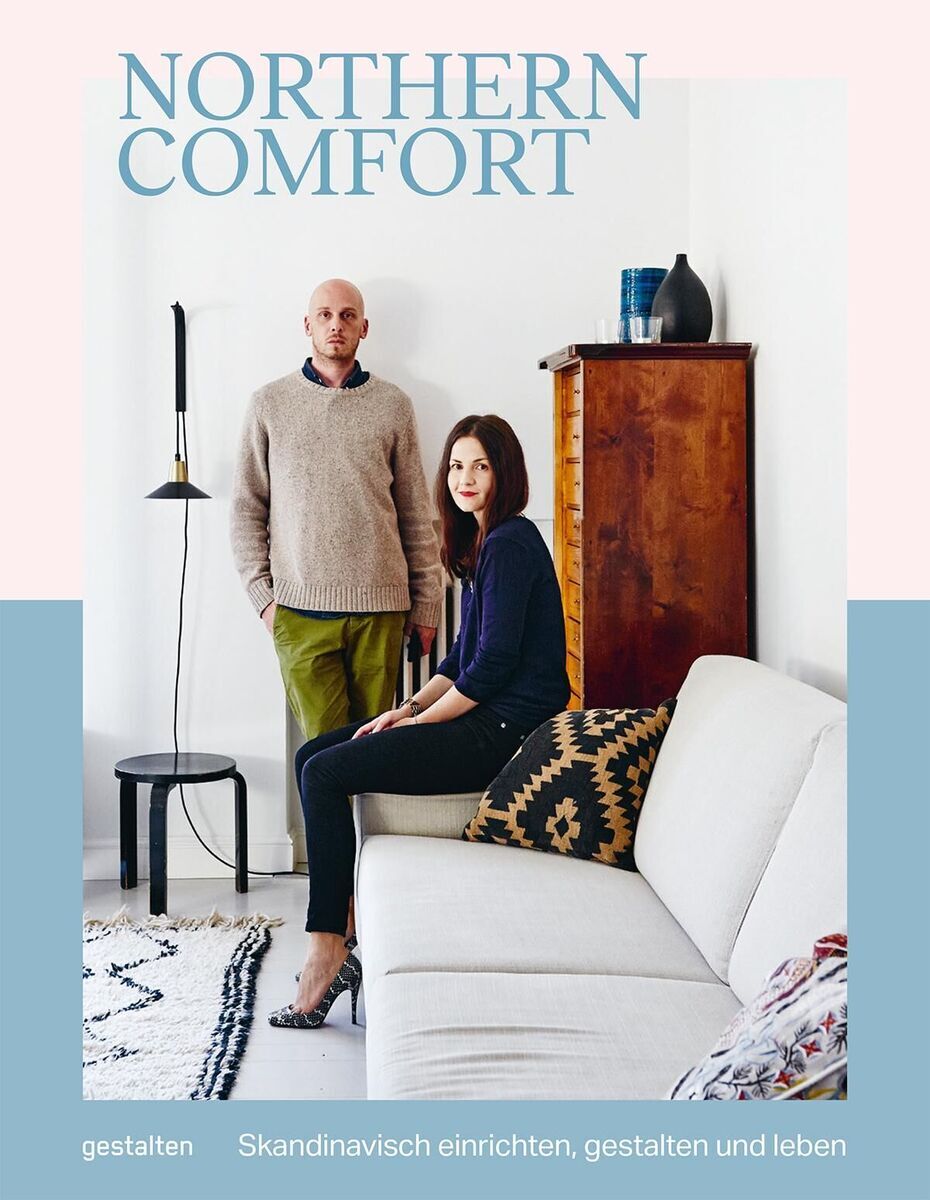 Zwei Personen stehen in einem skandinavisch eingerichteten Wohnzimmer, dekoriert mit einem weißen Sofa, einem Holzmöbelstück, einem modernen Teppich und minimalistischen Wohnaccessoires. Der Titel ‘Northern Comfort’ ist oben im Bild zu sehen.