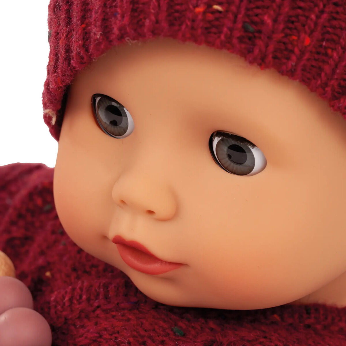 Großaufnahme einer liebevoll gestalteten Babypuppe mit einem gestrickten bordeauxroten Mützchen und passender Kleidung, geeignet als Kuschelpuppe für Kinder.