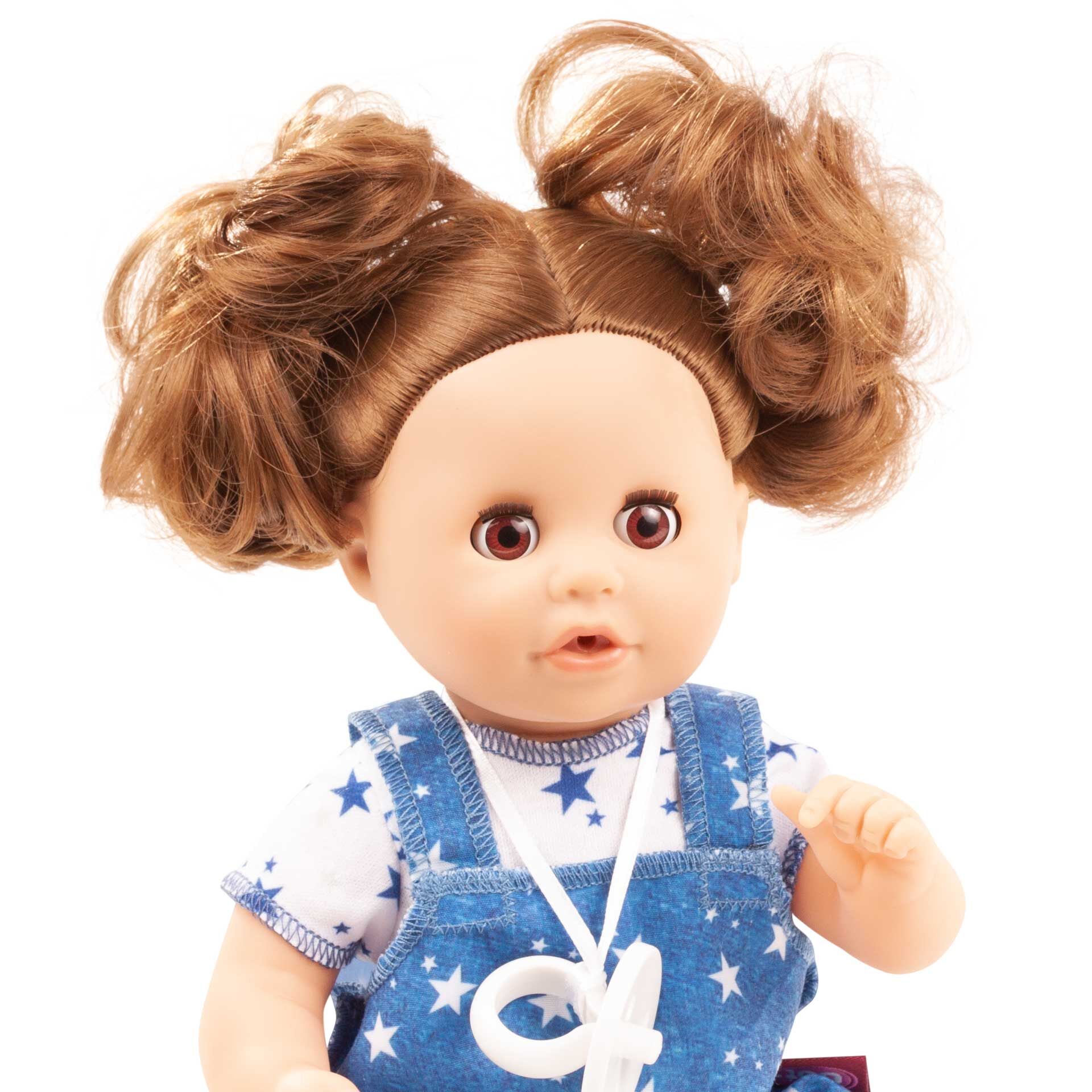 Die Badepuppe ‚Sleepy Aquini Girl Mein Stern‘ trägt einen blauen Overall mit weißen Sternen über einem weißen T-Shirt mit blauen Punkten. Die Puppe hat braune Haare, die zu zwei Zöpfen frisiert sind. Um ihren Hals hängt ein weißer Schnuller an einem Band. Die Puppe steht vor weißem Hintergrund.