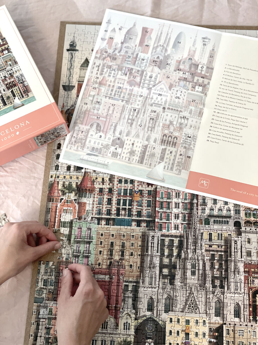 Zwei Hände setzen ein Puzzle mit 1000 Teilen zusammen, das eine detaillierte und farbenprächtige Darstellung von Barcelonas Architektur zeigt. Neben dem Puzzle liegt eine Anleitung mit einer Übersicht des fertigen Bildes und Beschreibungen der dargestellten Gebäude.