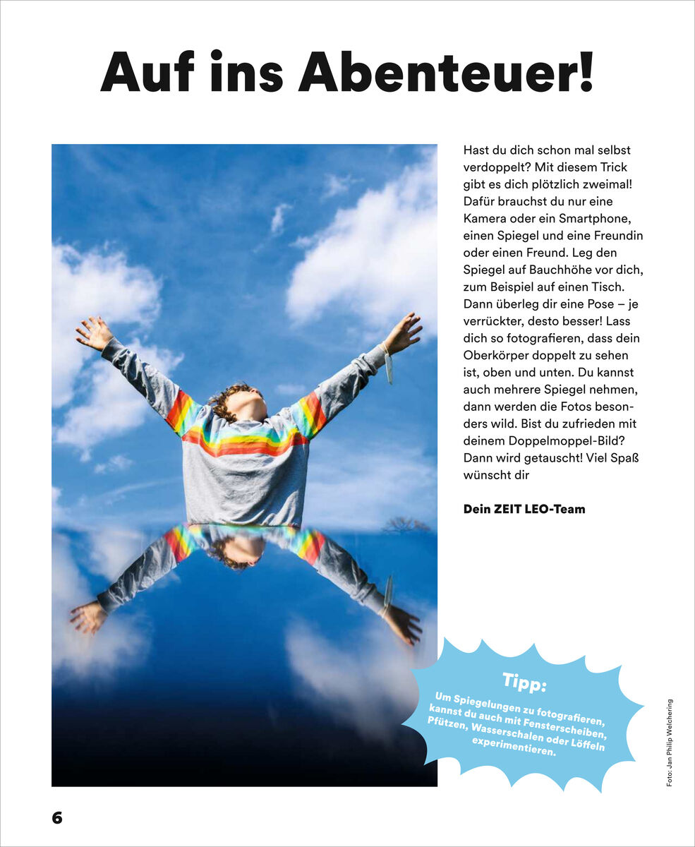 Eine Kinderzeitschriftenseite mit großem Foto: Ein Kind mit Regenbogenpulli streckt die Arme vor blauem Himmel aus. Unter ihm spiegelt ein klarer Spiegel das Bild. Überschrift: "Auf ins Abenteuer!" Text erklärt, wie man witzige Doppelgänger-Fotos mit Spiegeln machen kann.