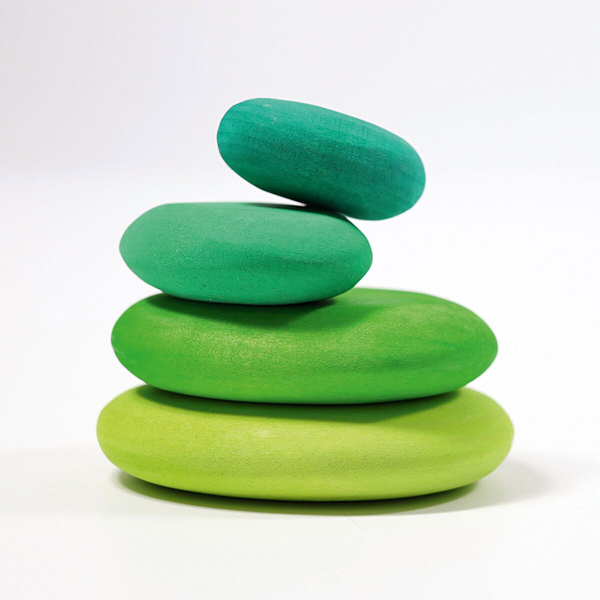 Vier unterschiedlich große, grüne Holzsteine der Marke GRIMM’S sind aufeinander gestapelt. Die Steine sind glatt, organisch geformt und farblich lasiert, von hellgrün bis dunkelgrün, und liegen auf einer weißen, neutralen Fläche.