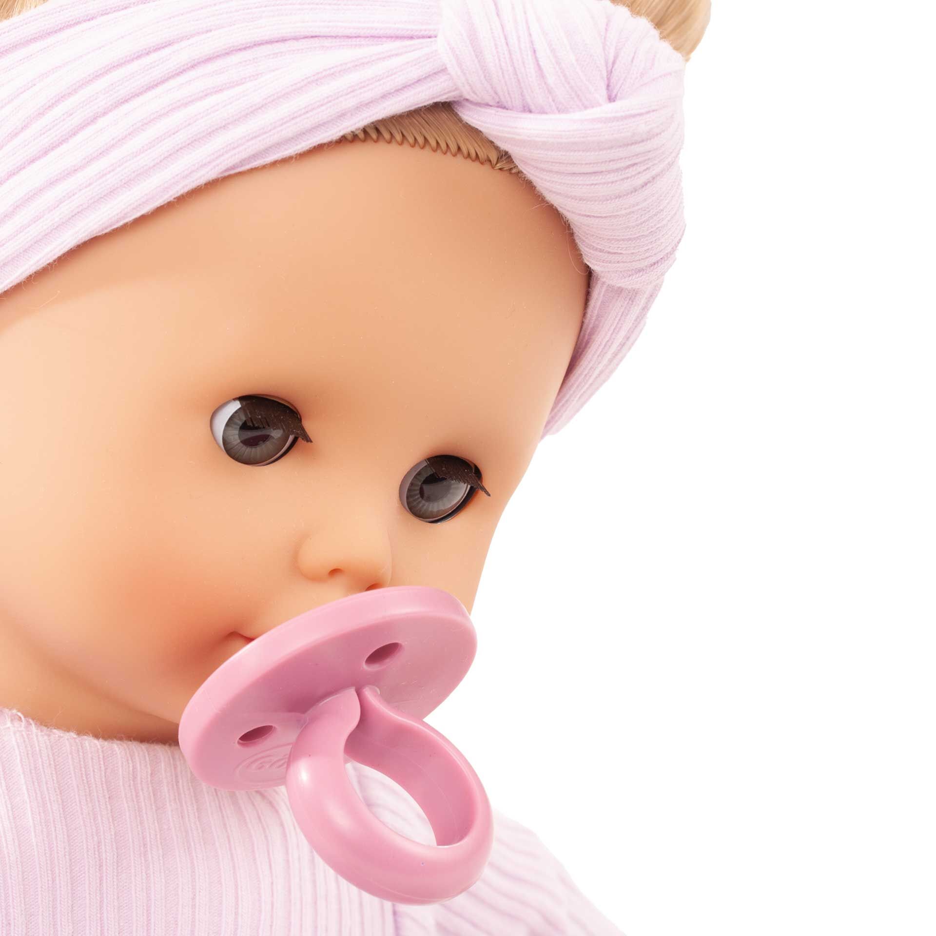 Nahaufnahme einer Babypuppe namens »Muffin BliBlaBlume« mit rosa Stirnband und passendem Schnuller. Die Puppe trägt ein gestreiftes Oberteil und richtet ihren Blick leicht zur Seite.