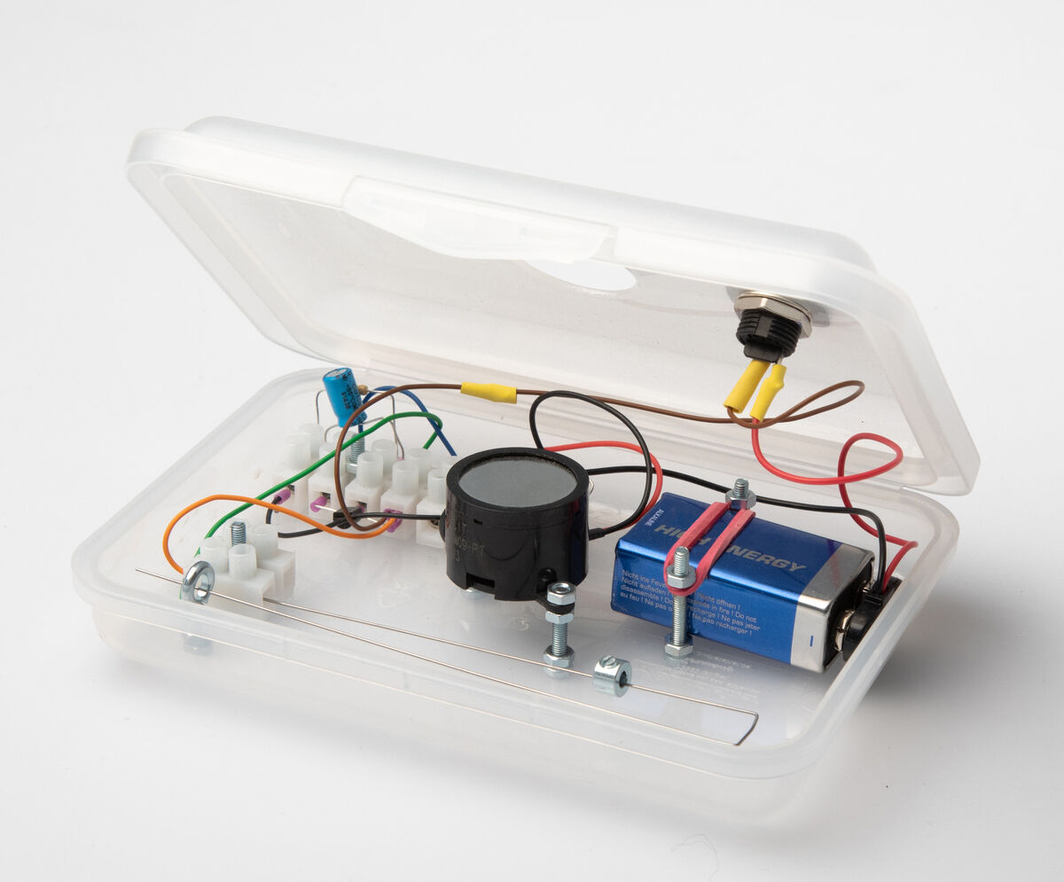 Experimentierkasten genannt »Bewegungsalarm« mit Elektronik-Bauteilen wie Batterien, Drähten, Schaltkreisen und Sensoren in einem transparenten Kunststoffgehäuse.