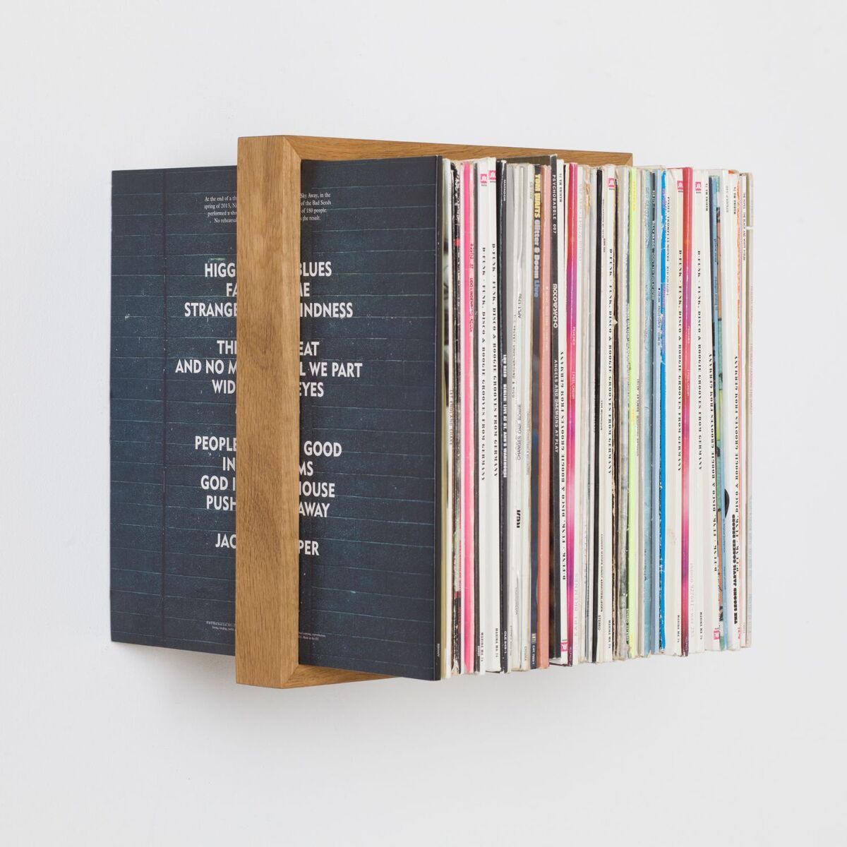 Ein wandmontierter Plattenständer, Produktbezeichnung 'b-platte', hält eine Sammlung von Schallplatten. Der Halter besteht aus Holz und ist schlicht und minimalistisch gestaltet.
