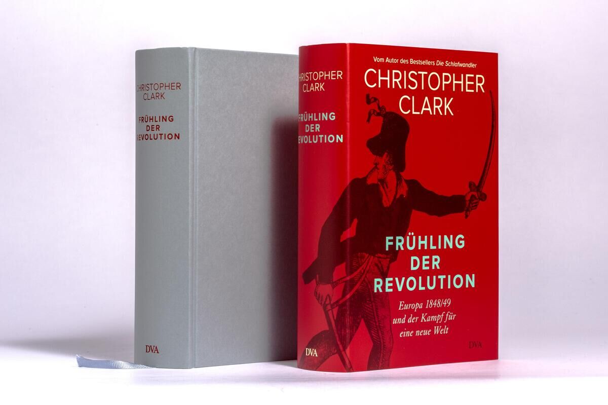 Zwei Bücher von Christopher Clark mit dem Titel 'Frühling der Revolution' im Vordergrund. Eines der Bücher hat einen roten Schutzumschlag mit schwarzem Text und einer historischen Abbildung. Das andere Buch ist grau mit rotem Text.