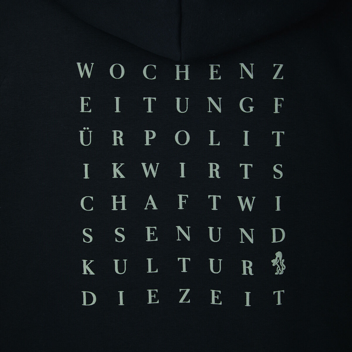 Ein schwarzer Hoodie der ZEIT Kollektion mit einem Rückendruck, der aus weißen Buchstaben besteht, die wie ein Worträtsel angeordnet sind. Die Buchstaben bilden Wörter wie „WOCHENZEITUNG,” „POLITIK,” „WISSENSCHAFT” und „KULTUR.