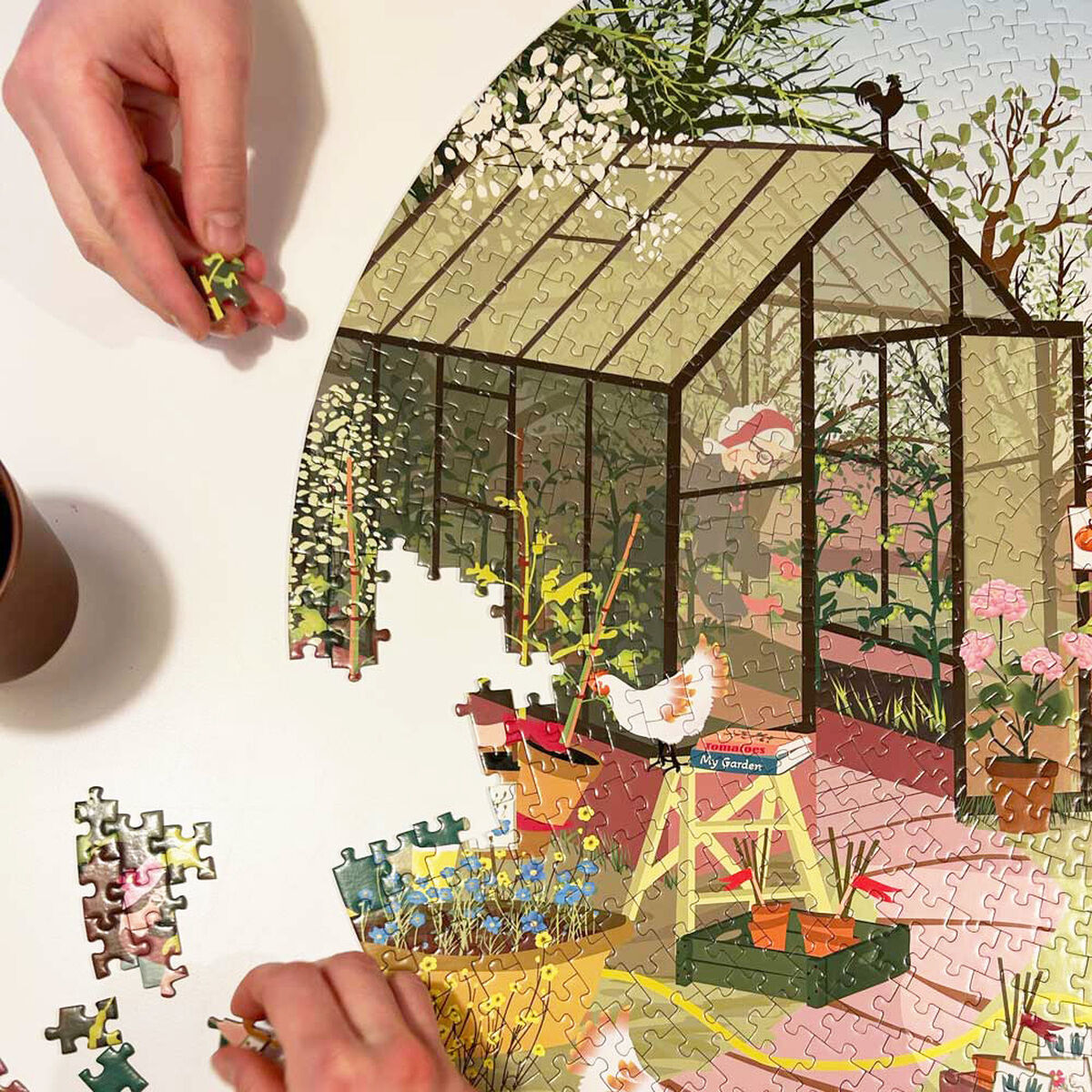 Ein Puzzle mit dem Thema Frühlingsgefühl zeigt ein idyllisches Bild eines Gartens mit einem Gewächshaus und Hühnern. Das fotografierte Puzzle wird von Händen zusammengefügt.