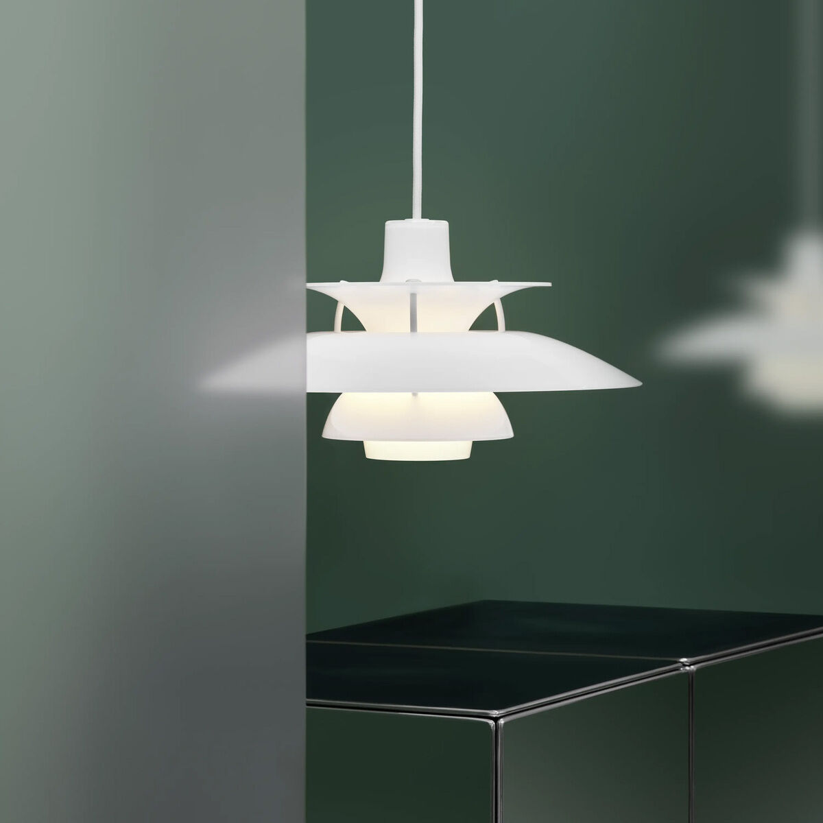 Moderne weiße Hängeleuchte »PH 5 320« von Louis Poulsen hängt in einem schlichten, eleganten Raum mit dunkler Wand und glänzendem Sideboard. Die mehrfach geschichteten Schirme sorgen für blendfreies Licht. Minimalistische und stilvolle Raumatmosphäre.