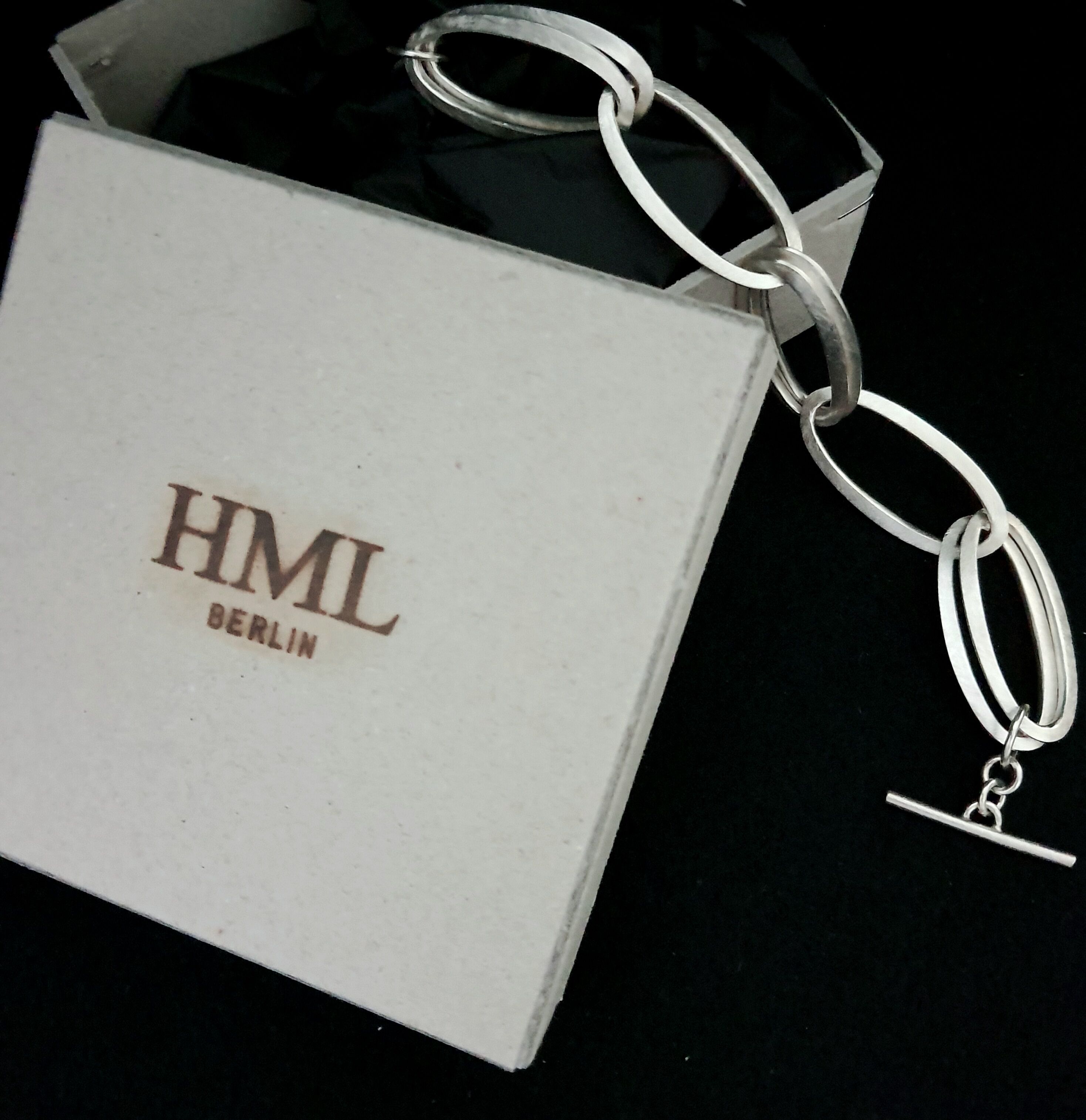 Silberne Kette mit großen, ovalen Gliedern neben einer weißen Verpackung mit braunem Schriftzug 'HML BERLIN'