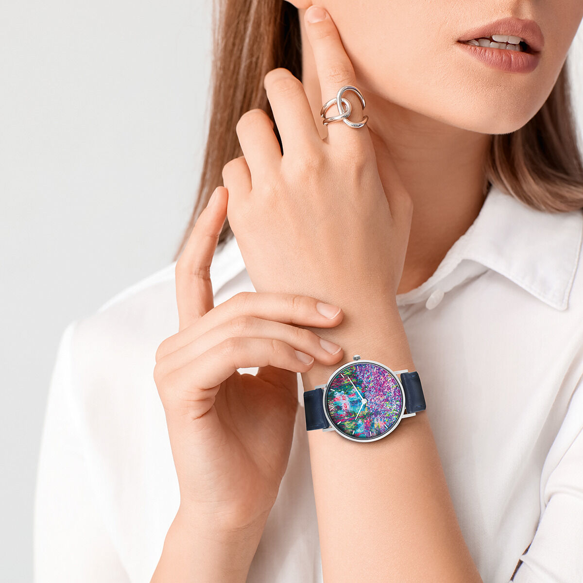 Eine elegante Armbanduhr mit einem farbenfrohen Zifferblatt, inspiriert von Monets Gemälde 'Irisbeet in Monets Garten'. Die Uhr wird von einer Frau mit einem weißen Hemd getragen, und das Design zeigt viele bunte Akzente.