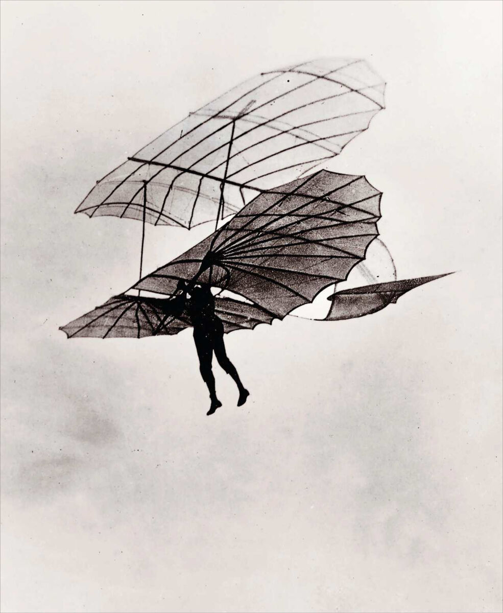 Historisches Schwarz-Weiß-Foto eines frühen Fluggeräts mit einer Person, die an filigranen, vogelähnlichen Flügelkonstruktionen in der Luft hängt. Die feinen Strebensegmente und die dynamische Pose visualisieren den Pioniergeist der frühen Luftfahrt.