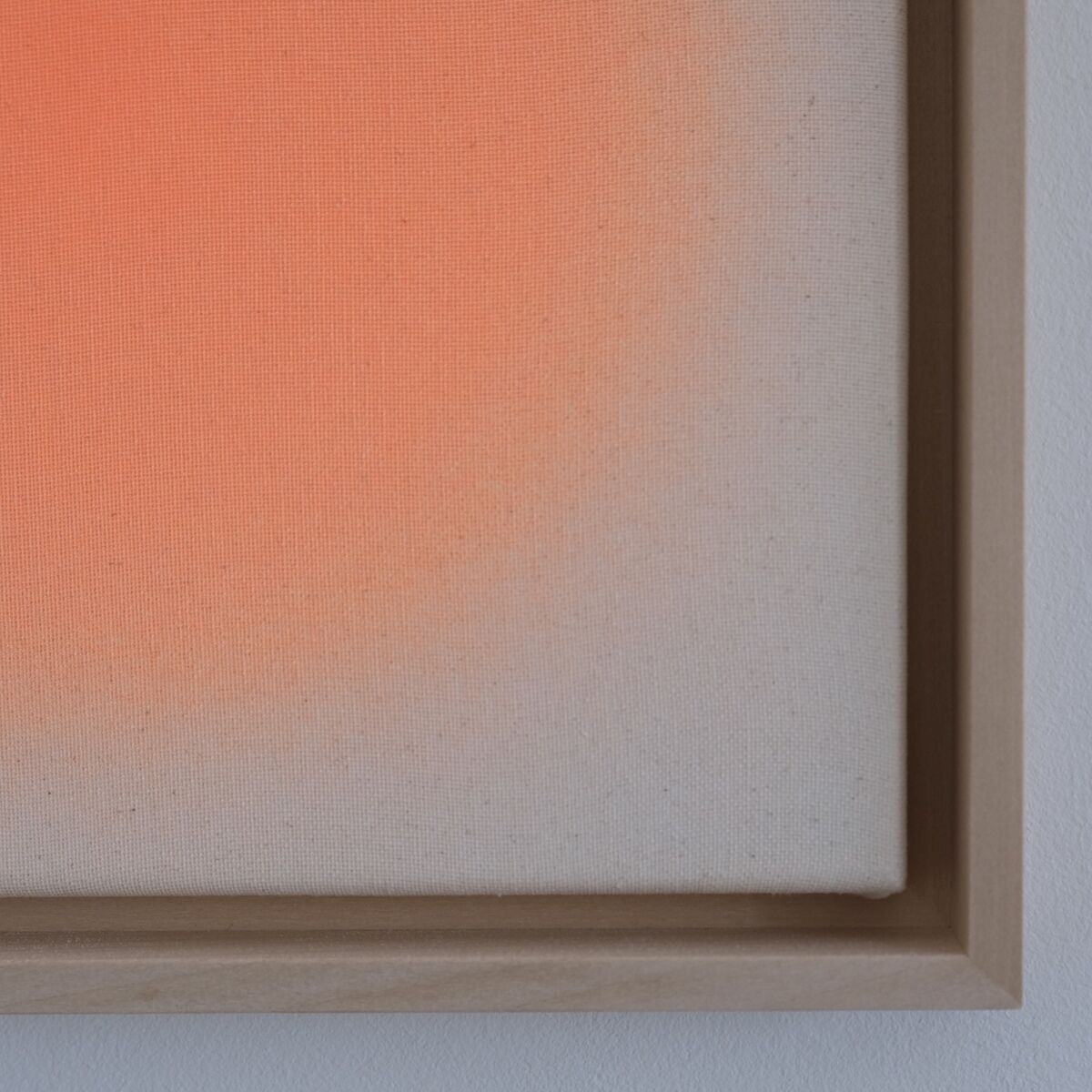 Quadratisches Wandbild im Format 30x30 cm, mit sanftem orangefarbenem Verlauf auf weißer Leinwand in einem hellbraunen Holzrahmen. Das minimalistische Kunstwerk strahlt eine moderne und beruhigende Atmosphäre aus und ist an einer weißen Wand ausgestellt.