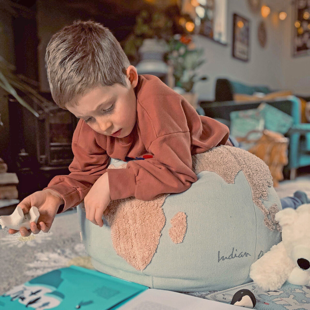 Ein Kind liegt auf einem Sitzkissen in Form eines Poufs mit Weltkartenmotiv und liest ein Buch in einem gemütlich dekorierten Raum.