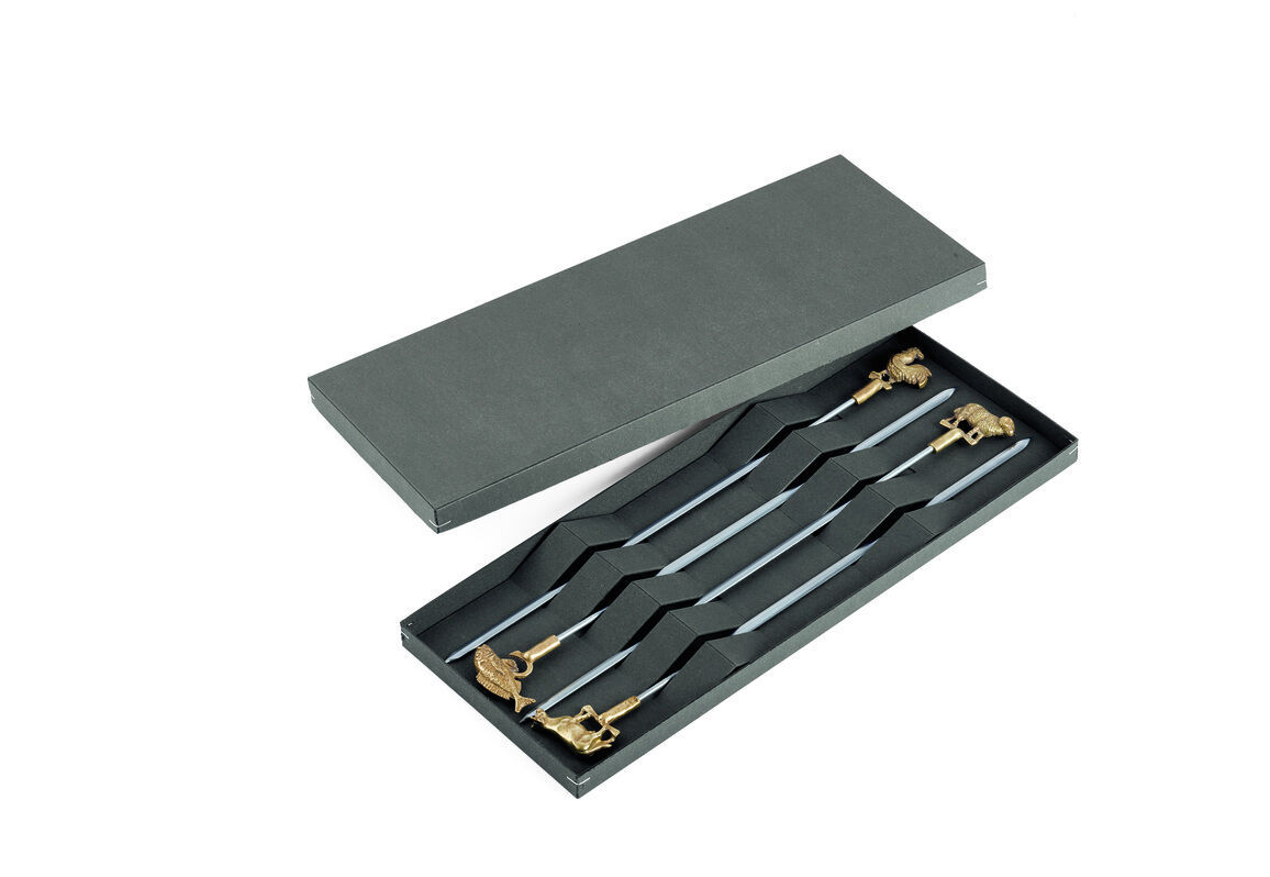 Ein Set aus Edelstahl-Grillspießen in einer schwarzen Schachtel mit goldenen Verzierungen an den Griffen.