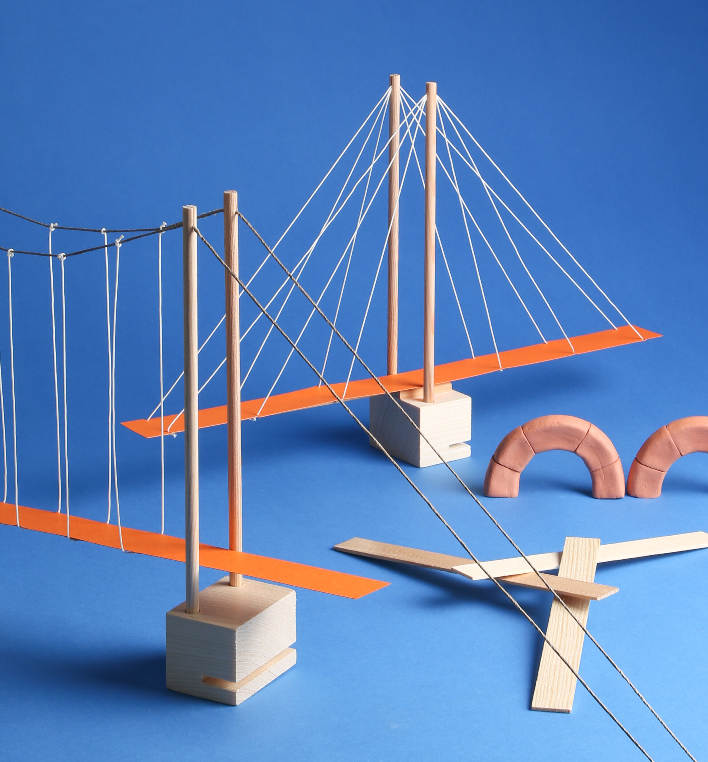 Verschiedene Brückenmodelle aus Holz und Fäden, zusammengesteckt auf einem blauen Hintergrund. Die Konstruktionen sind Teil eines Baukastens zum Thema Brückenbau und dienen als Lernspielzeug für Kinder oder für den Schulunterricht.