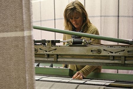Frau bedient eine große Strickmaschine in einer Textilfabrik