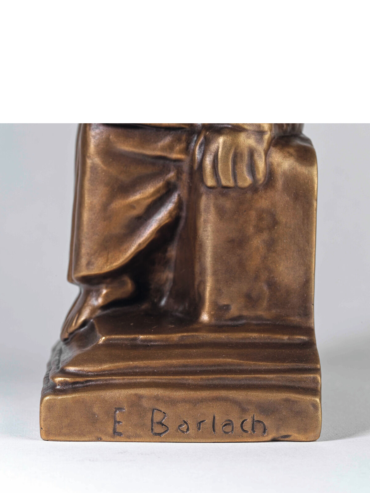 Skulptur von Ernst Barlachs 'Lesender Klosterschüler', 1930. Die Bronzeplastik zeigt die untere Körperhälfte eines sitzenden Schülers, der ein Buch liest. Der Sockel trägt die Signatur 'E Barlach'.