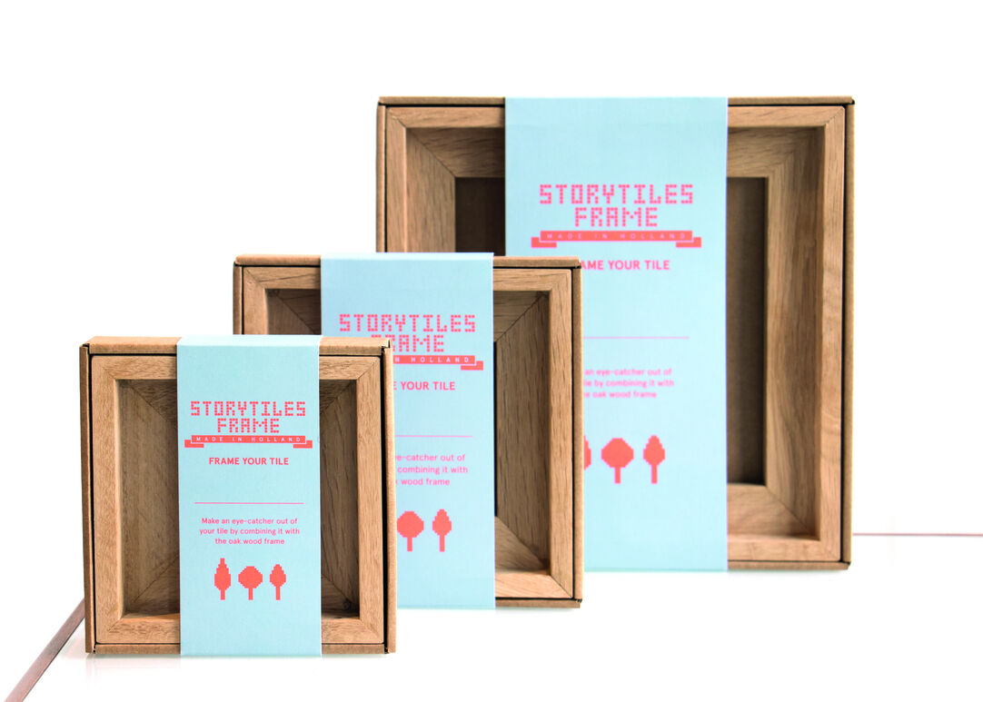 Drei Holzrahmen von StoryTiles in verschiedenen Größen. Jeder Rahmen hat eine türkisfarbene Verpackung mit rosa und schwarzen Akzenten. Die Schichtung und die handgefertigte Natur des Produkts sind deutlich sichtbar.