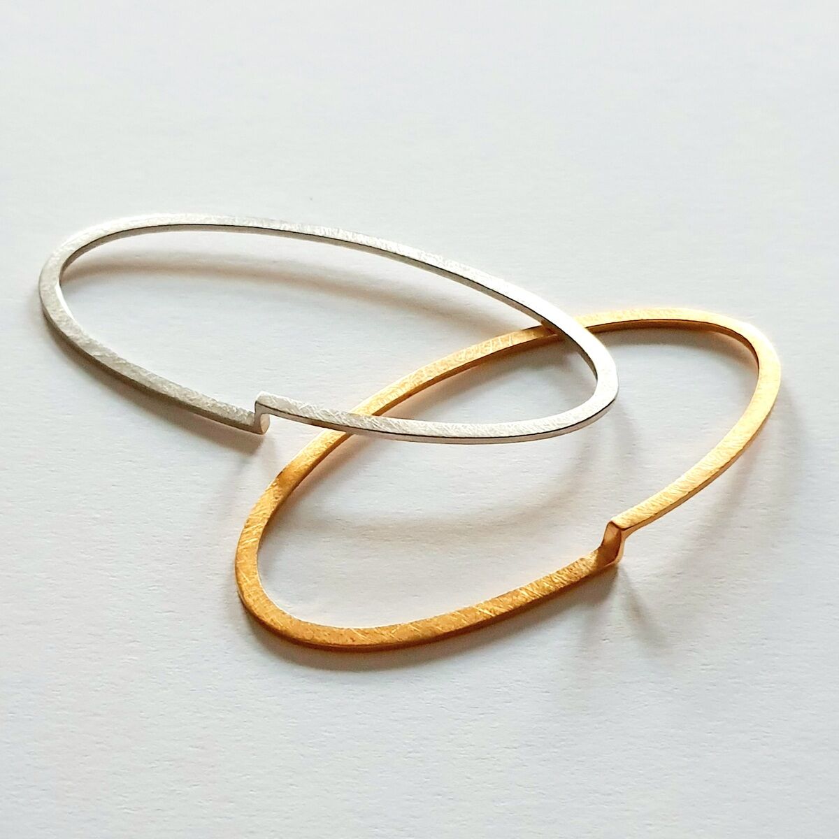Zwei schlichte Armreifen auf hellem Hintergrund, einer in Gold- und einer in Silberoptik, in minimalistischem Design.