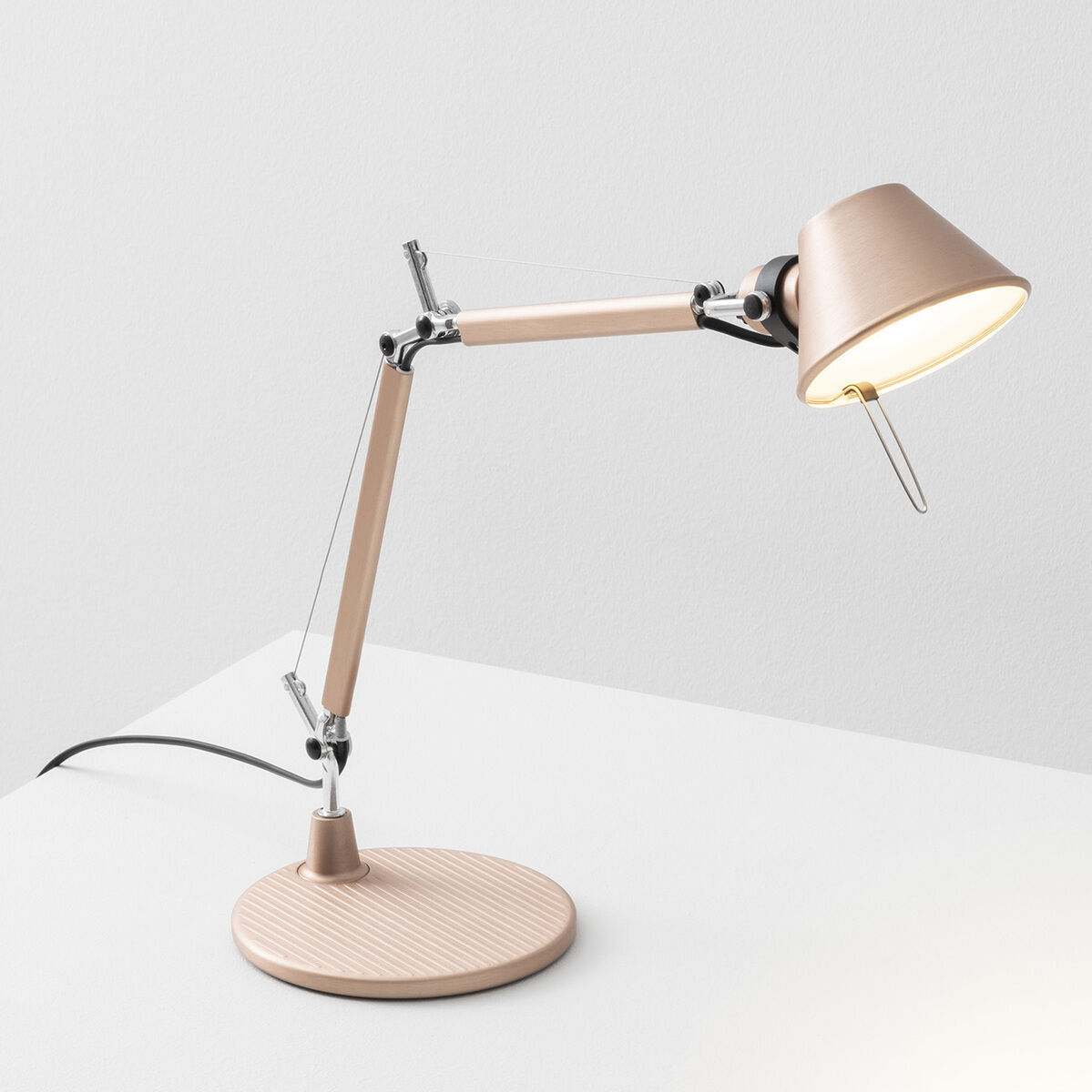 Ein modernes Bild einer beige Designer-Schreibtischlampe namens 'Artemide »Tolomeo Micro«' vor einem weißen Hintergrund. Die Lampe hat ein minimalistisches, funktionales Design mit verstellbaren Gelenken und einem runden Sockel.