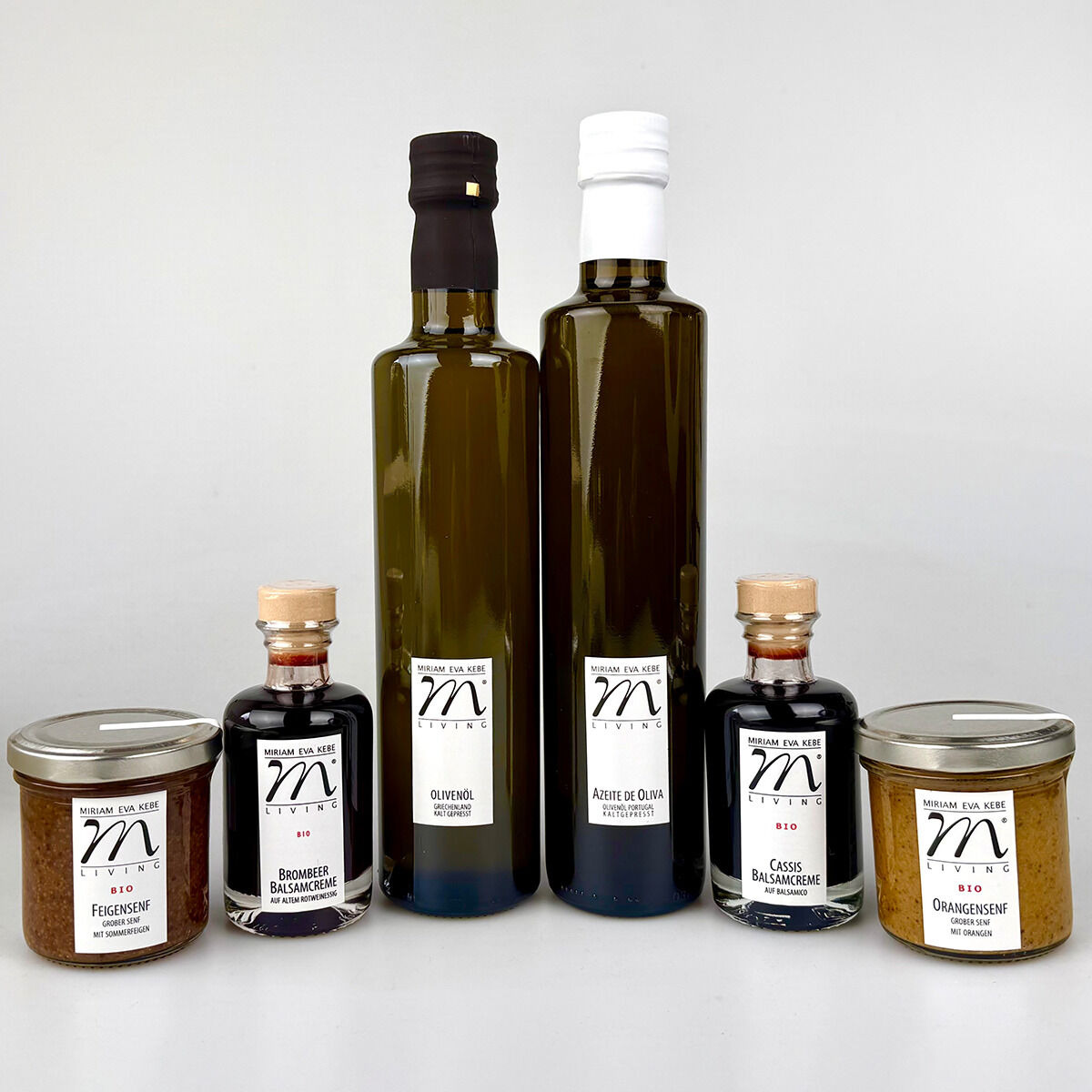 Sechs Feinkostprodukte des Gourmet-Sets »ZEIT für köstlichen Salat«: zwei grüne Olivenölflaschen (Portugal, Griechenland), zwei kleine Glasflaschen mit dunkler Balsamcreme (Brombeere, Granatapfel), zwei Gläser Bio-Senf (Feige, Orange) auf hellem Hintergrund, hochwertige Etiketten.