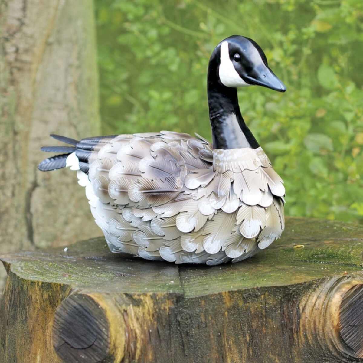 Gartenfigur Kanadagans auf einem Baumstumpf vor einer grünen, blättrigen Hintergrund.