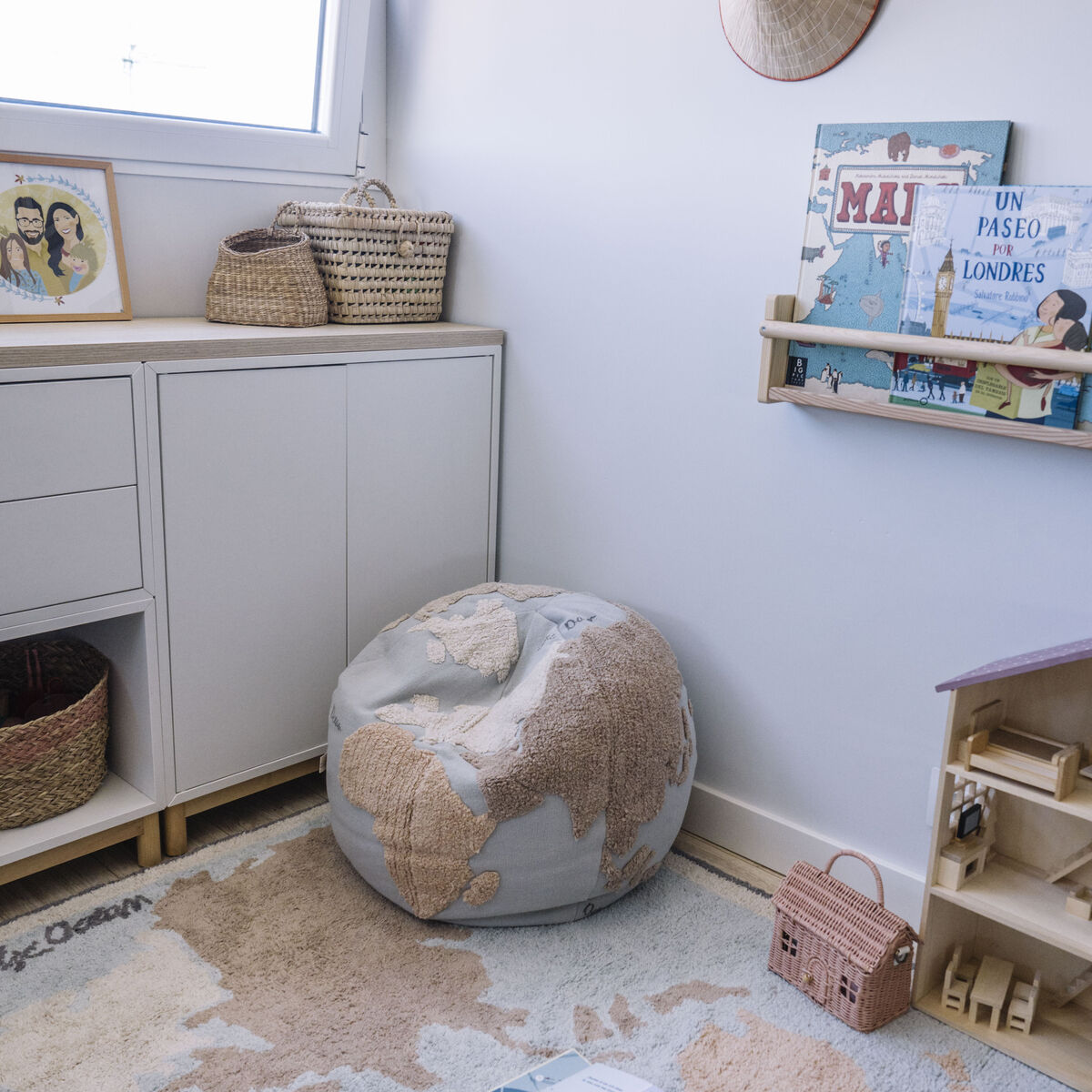 Ein Sitzkissen in Form eines Poufs mit Weltkartenmotiven, platziert in einem hellen und modernen Kinderzimmer. Das Zimmer ist mit Körben, Regalen und kindgerechten Büchern dekoriert.