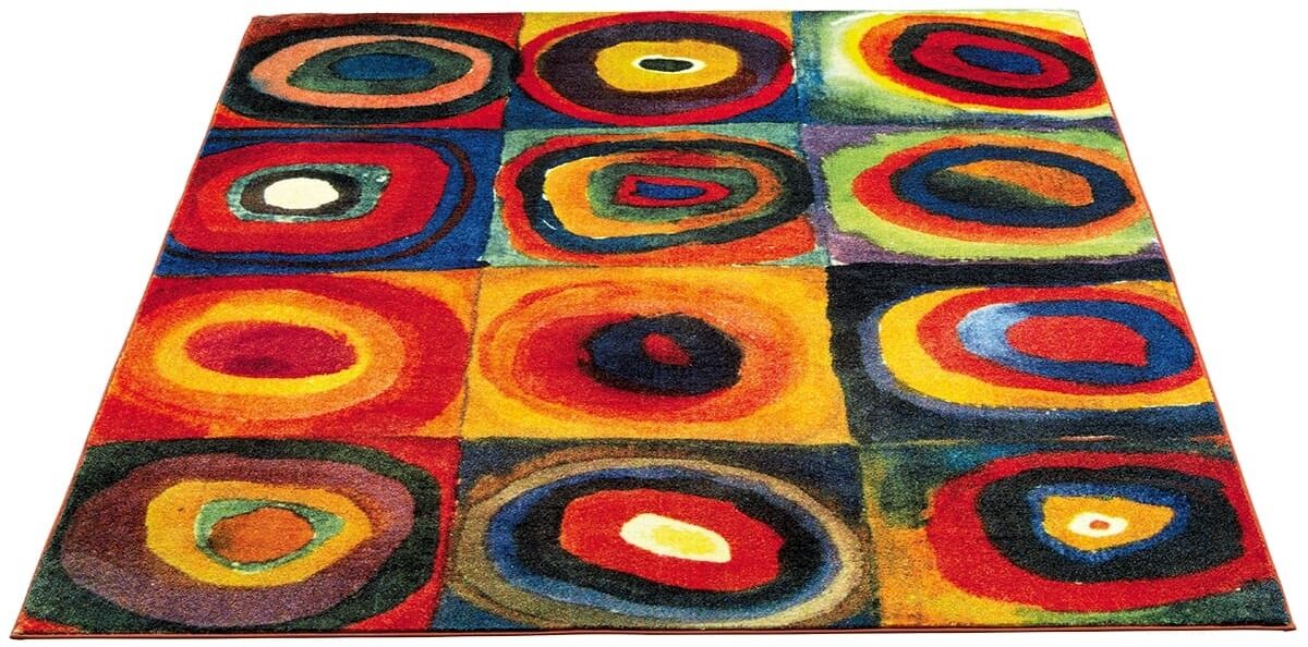 Ein bunter Teppich basierend auf der Farbstudie der Quadrate nach Kandinsky. Der Teppich zeigt ein geometrisches Muster mit vielfältigen, lebendigen Farben wie Rot, Orange, Gelb, Grün, Blau, Violett, Schwarz und Weiß.