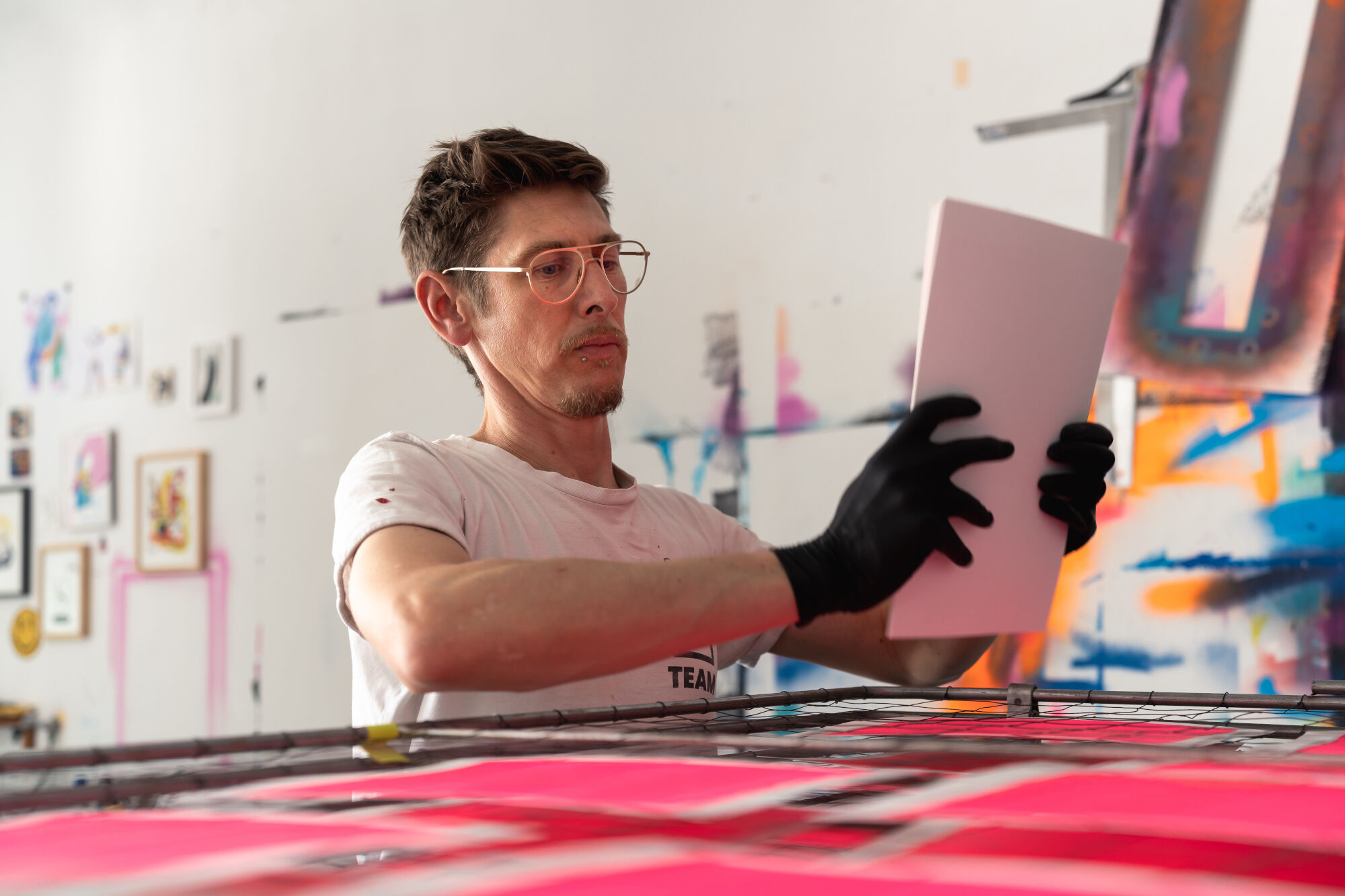 Person mit schwarzen Handschuhen hält rechteckiges weißes Objekt in einem Atelier mit bunten Wandmalereien