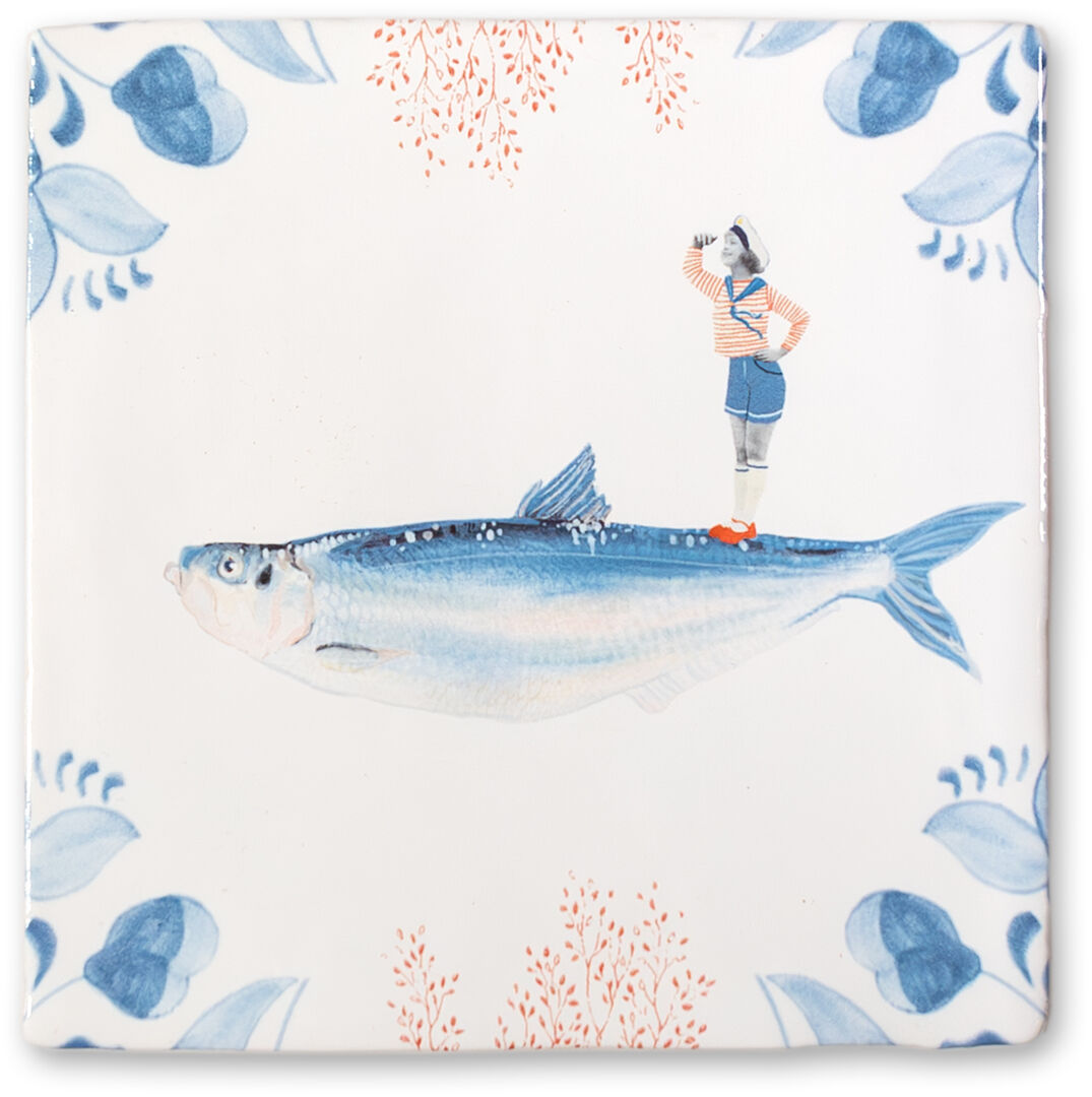 Keramikfliese mit einem großen Fisch und einer kleinen Figur eines Seemanns in einem gestreiften Hemd und blauer Hose, umgeben von blauen Blumenmustern auf weißem Hintergrund.