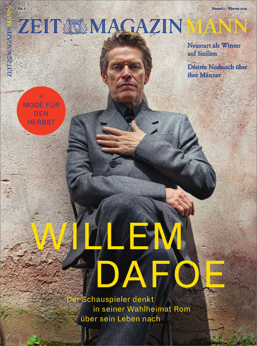 Cover des ZEITmagazin MANN 2/19. Das Titelbild zeigt einen älteren Mann, der einen grauen Anzug trägt. Er sitzt gegen eine hell-marmorierte Wand und hat die Hände vor der Brust verschränkt. Oben auf dem Cover stehen in blauer Schrift 'ZEITmagazin MANN', und im mittleren Teil steht in großer, gelber Schrift 'WILLEM DAFOE'. Im roten Kreis steht geschrieben 'Mode für den Herbst'.