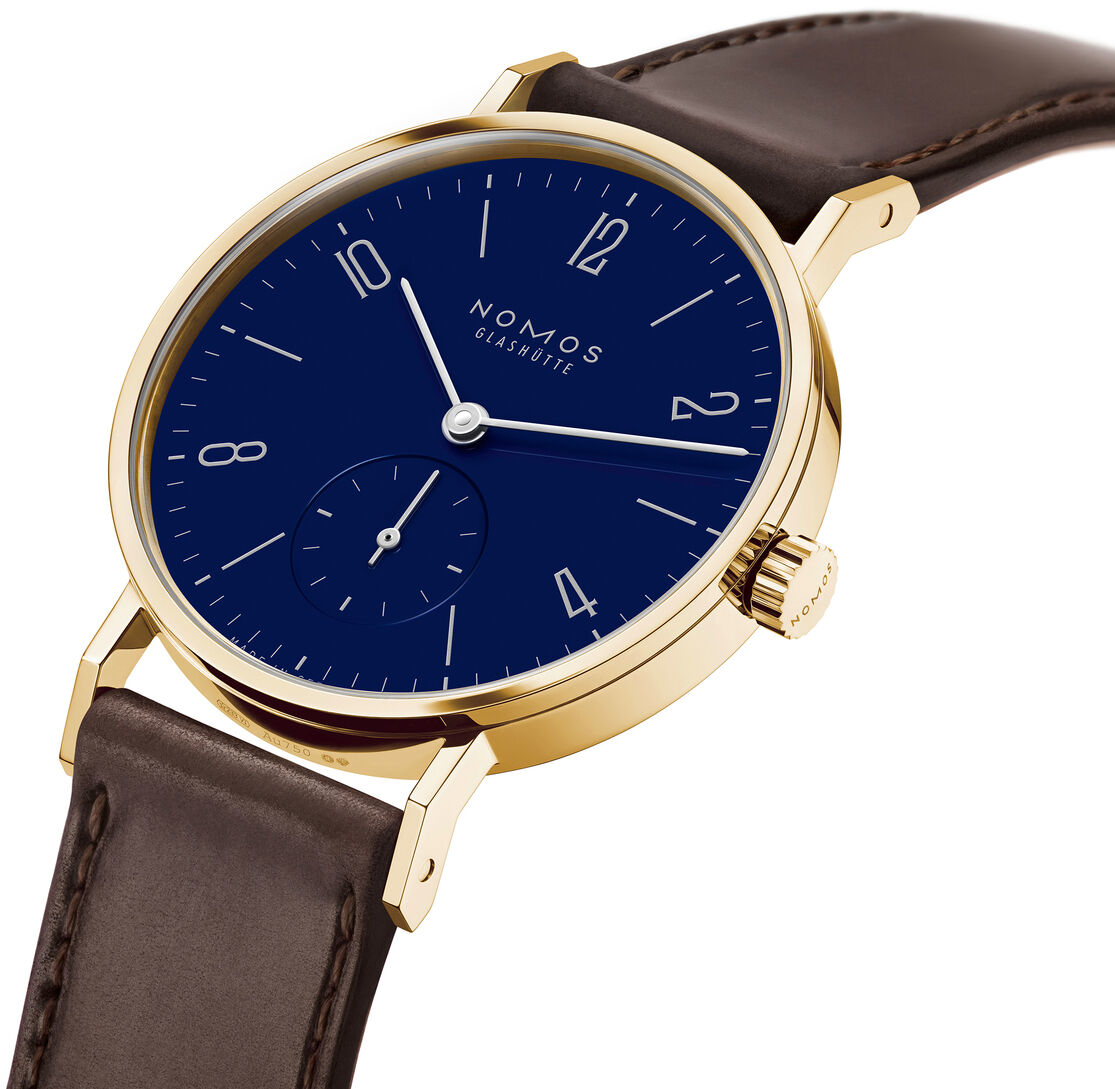 Die luxuriöse NOMOS ZEITmagazin-Sonderedition Tangente Gold 33 doré zeigt ein goldfarbenes Gehäuse mit emailleblauem Zifferblatt, klaren weißen Indizes und schlanken Zeigern. Das Armband aus dunkelbraunem Leder unterstreicht das exklusive, elegante Design der limitierten Armbanduhr.