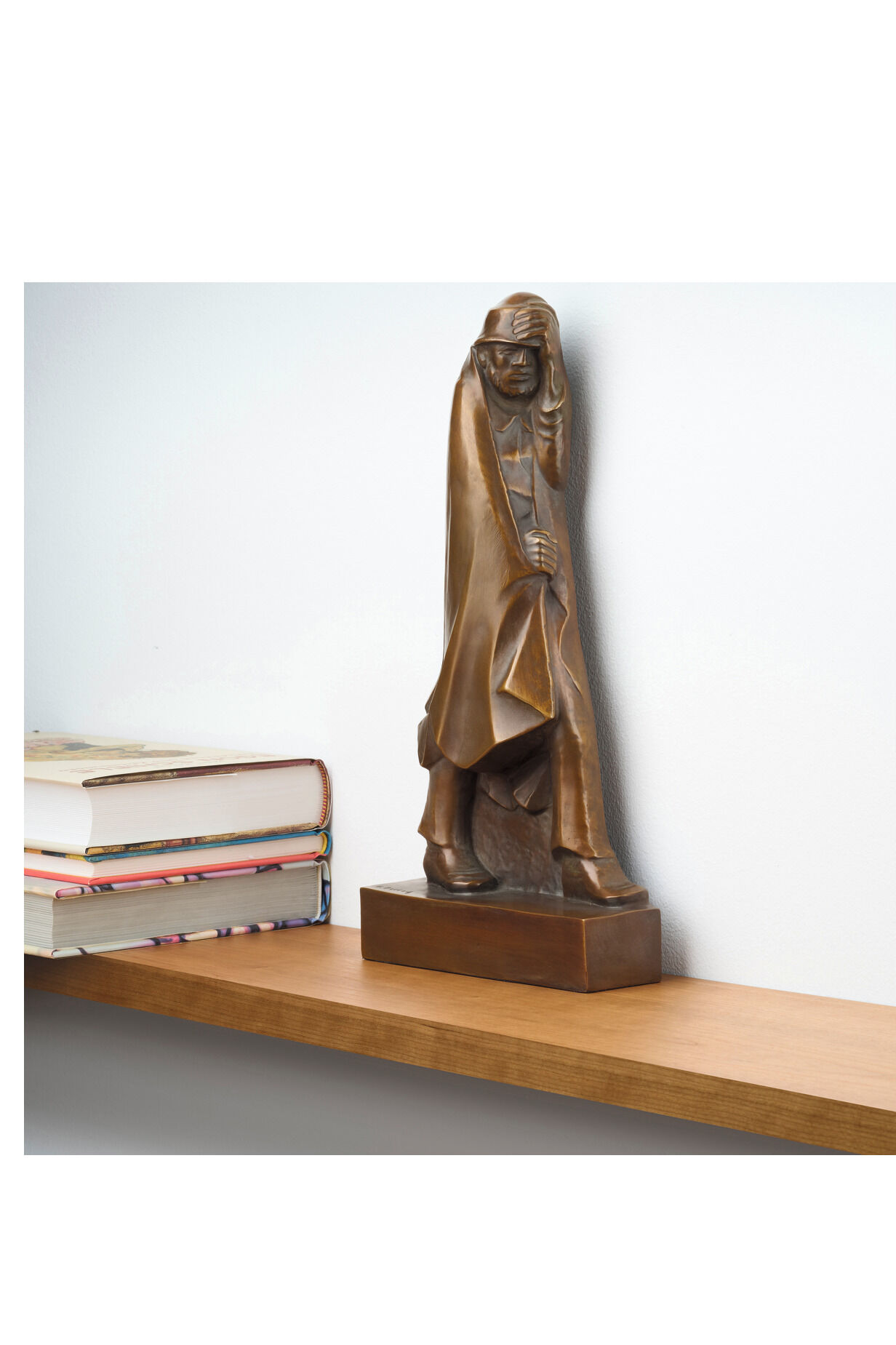 Bronzeskulptur »Wanderer im Wind« von Ernst Barlach auf einem Regal neben einem Stapel Bücher. Die Figur zeigt eine stilisierte Person im Wind, mit langer Kleidung und einem suggestiven Ausdruck.