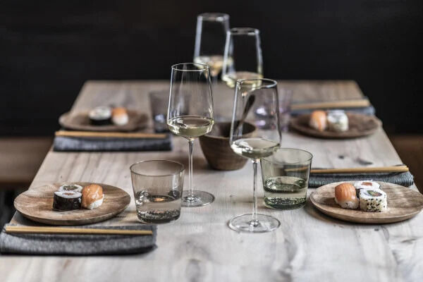 Ein gedeckter Tisch mit Weingläsern aus der Sommelier-Bundle-Serie »Vervino«, Holztellern, Sushi und grauen Stoffservietten.