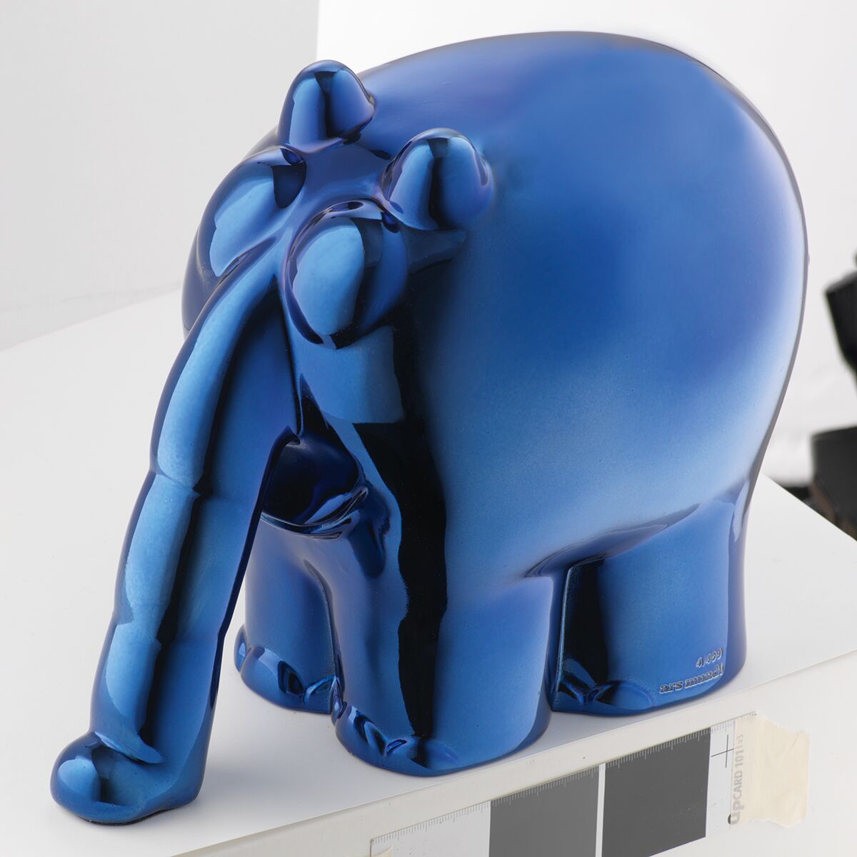 Eine glänzende Skulptur des Ottifanten von Otto Waalkes, gefertigt in Metallic-Blau aus Kunstguss. Die Skulptur zeigt einen stilisierten Elefanten mit verlängertem Rüssel in comicartigem Design. Im Hintergrund ist eine weiße, minimalistische Umgebung erkennbar, daneben ein Farbmusterstreifen.